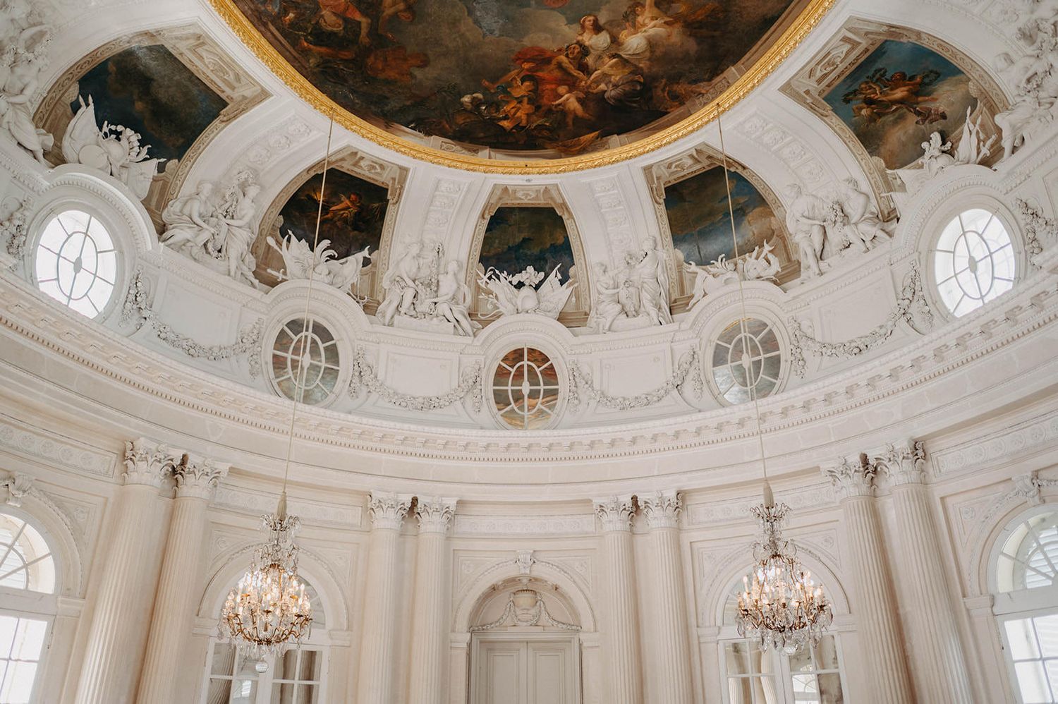 Ornate baroque dome interior with crystal chandeliers and white walls decorated with elaborate architectural details.
