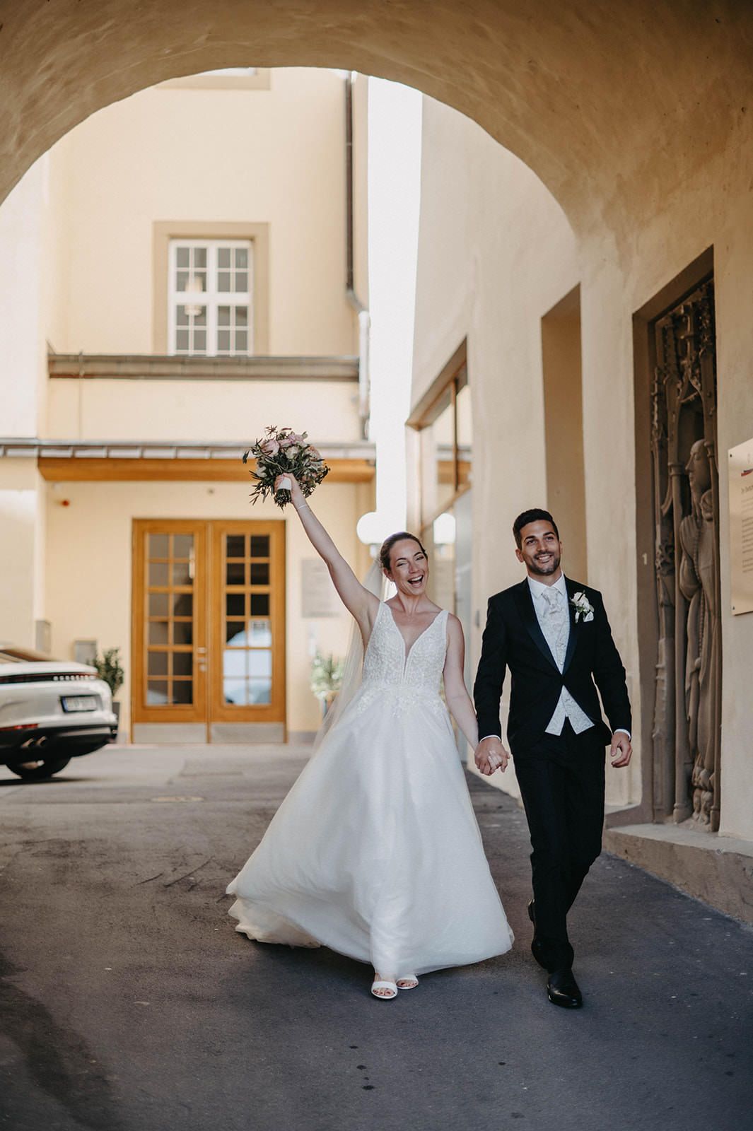 A bride and groom celebrate joyfully while walking under an arched passageway at their wedding venue.