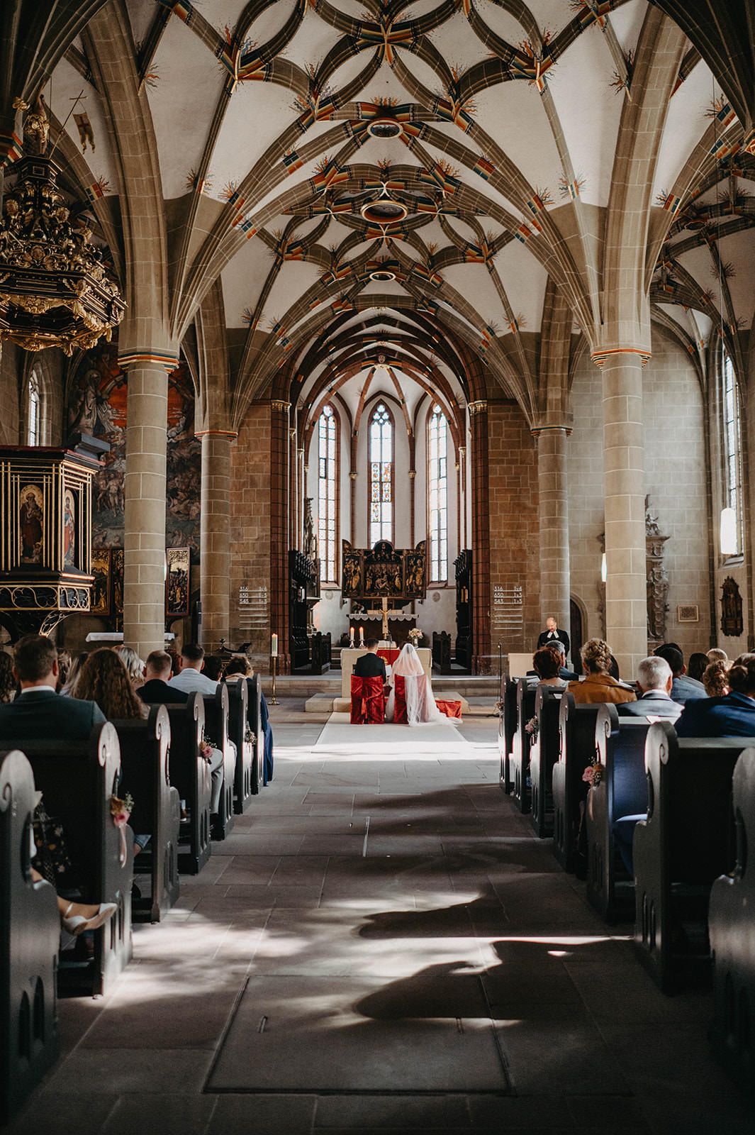 Historic stone hall with vaulted ceilings and columns showing guests gathered for a ceremony in natural light.