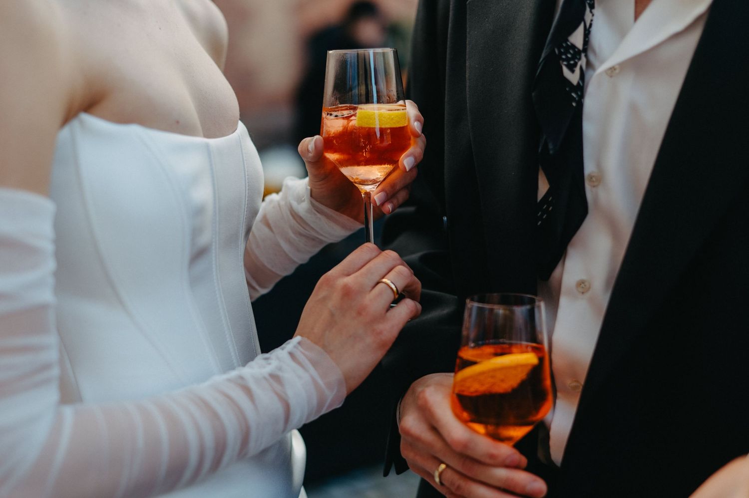 People in formal attire hold glasses of aperol spritz cocktails during an elegant event.