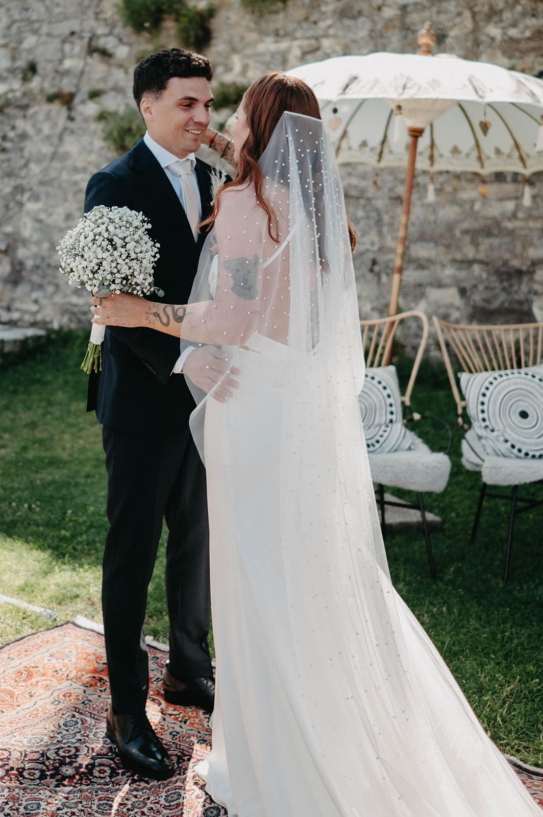 A couple shares a romantic moment during their outdoor garden wedding with white umbrellas and vintage decor.