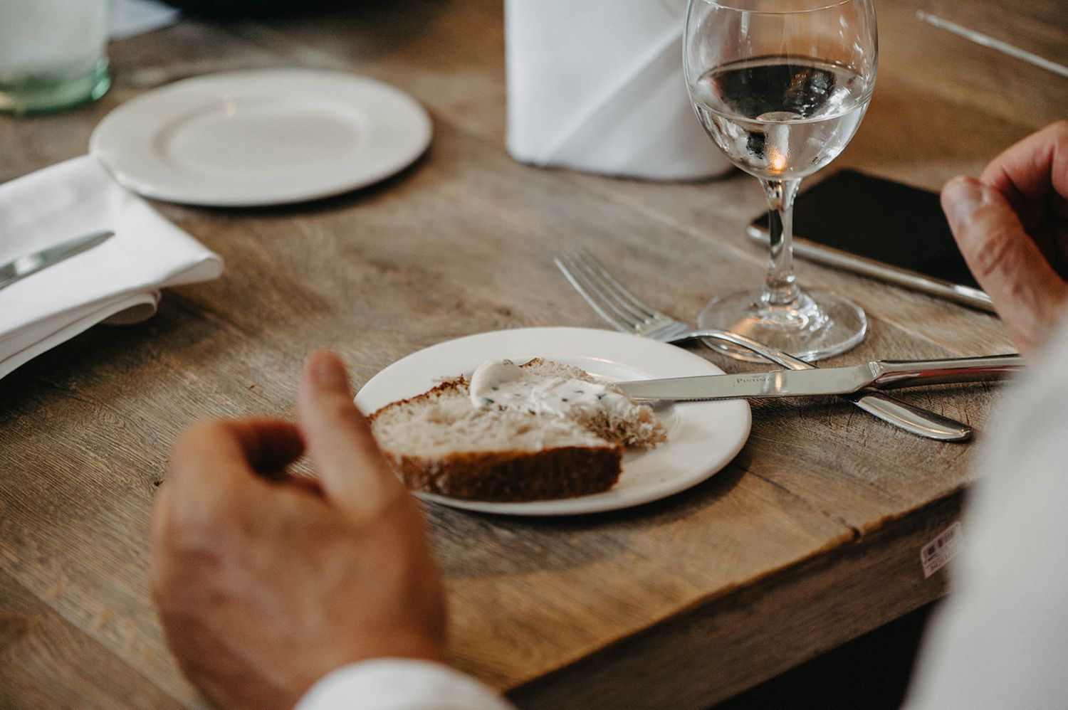Wooden dining table set with white plates and wine glasses in a rustic setting.