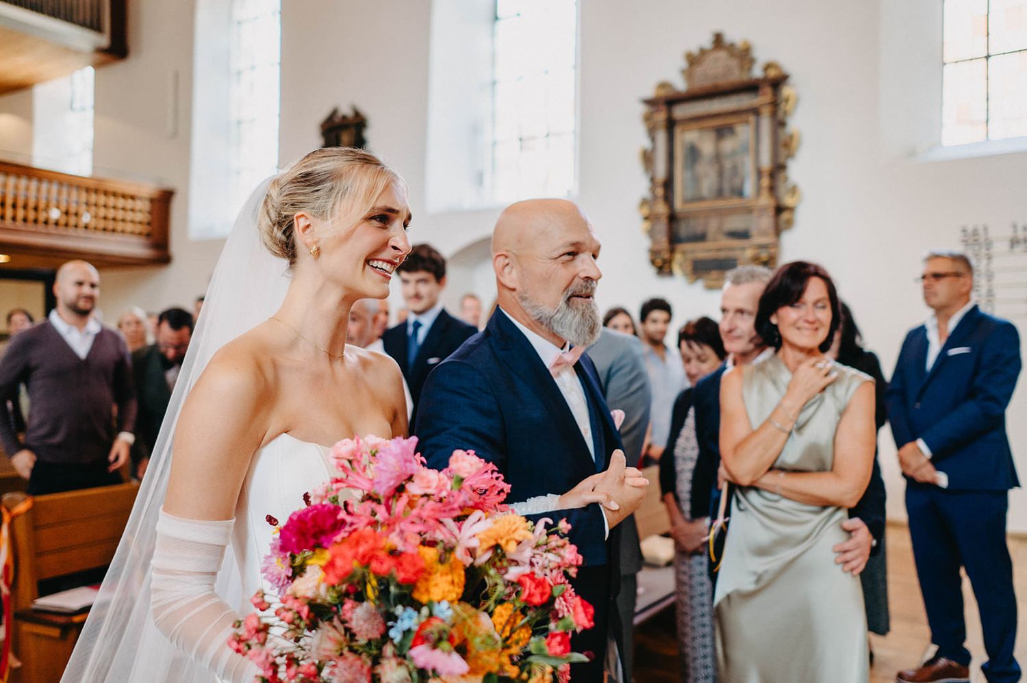 Joyful moment during church wedding ceremony with vibrant pink and orange floral bouquet.