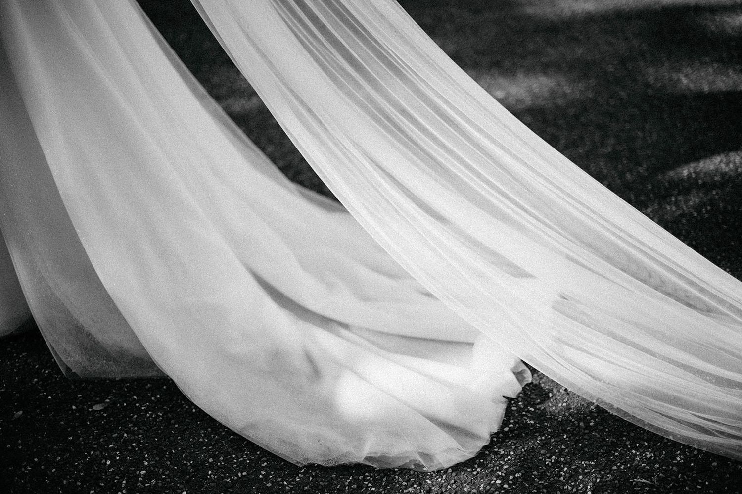 Elegant white wedding dress train draped gracefully across dark ground in black and white photography.