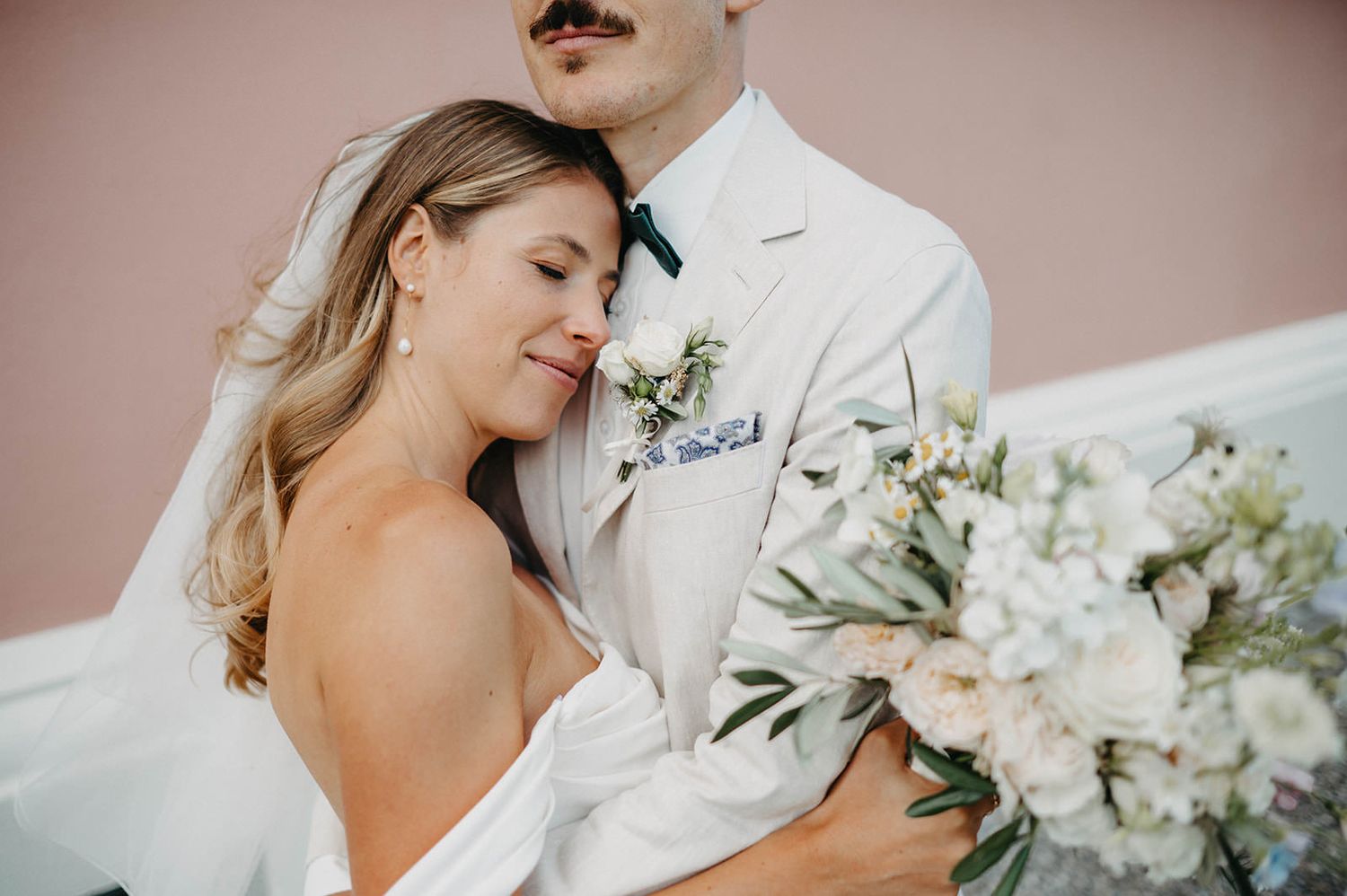 A romantic wedding couple embraces during their ceremony surrounded by elegant white floral arrangements.