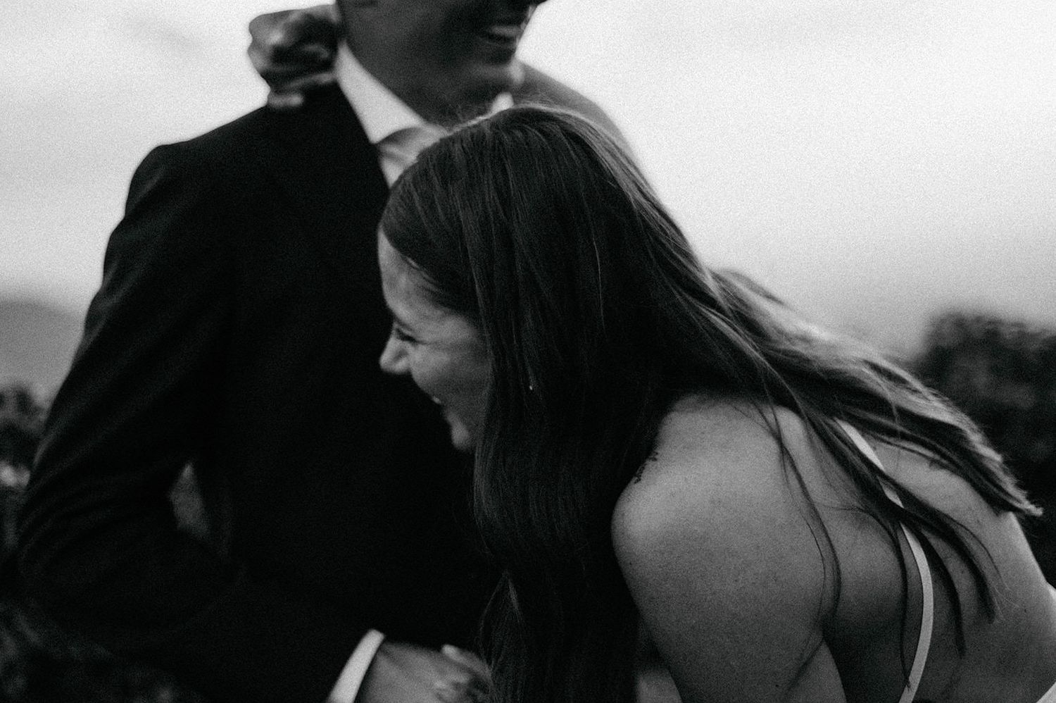 A candid black and white photograph captures a joyful moment between two people outdoors.