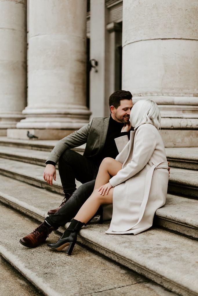 Romantic couple sitting on stone steps in elegant attire.