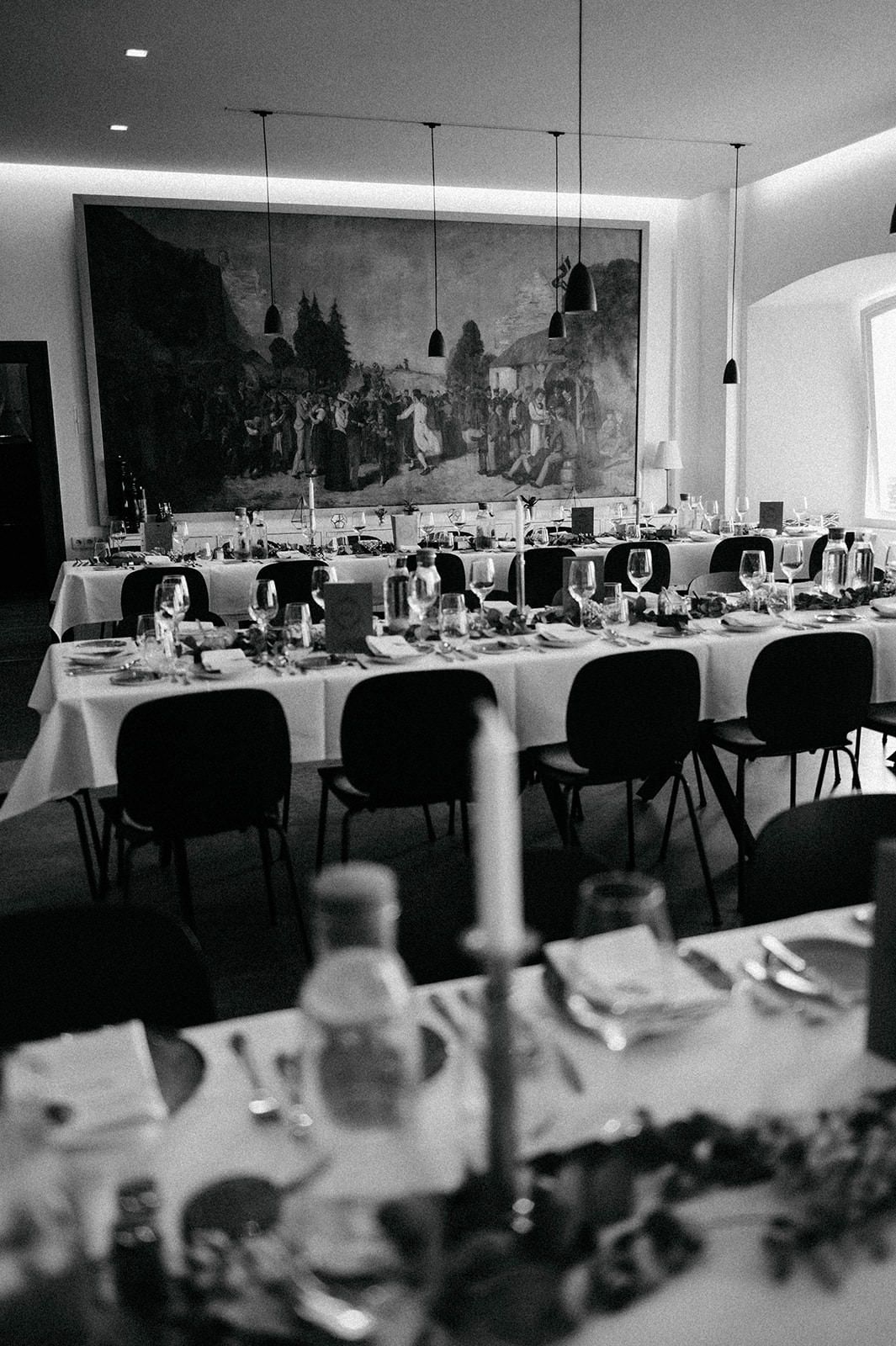 Black and white panoramic view of an elegant restaurant dining room with white tablecloths and pendant lighting.