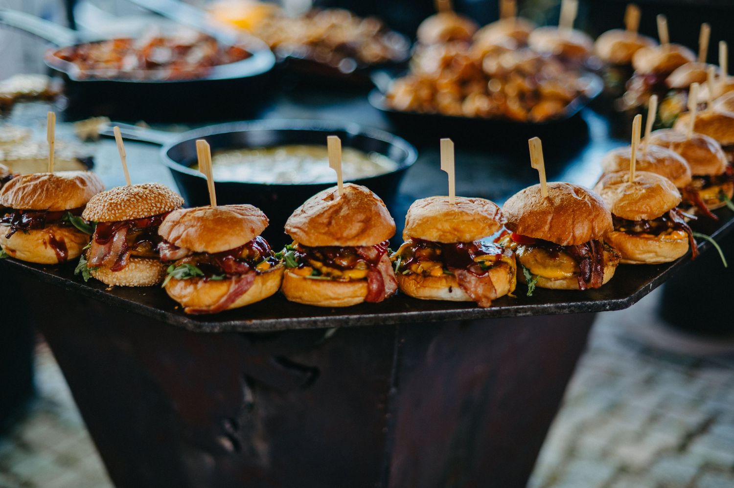 Rows of gourmet mini cheeseburger sliders with toasted buns arranged on black serving platters.