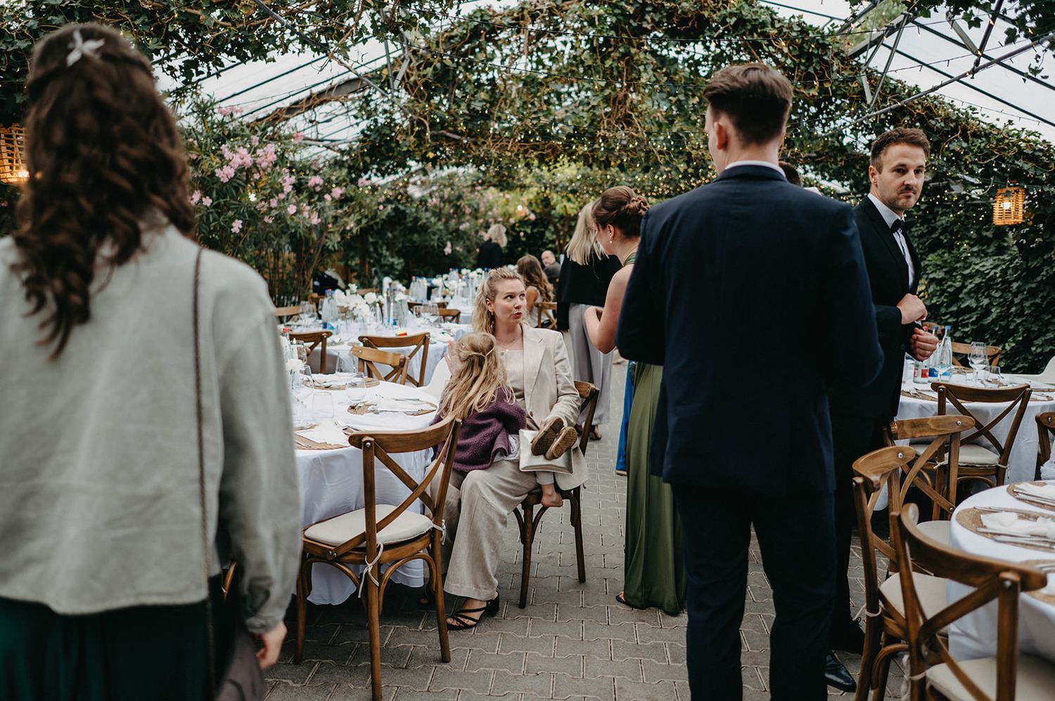 Wedding guests mingling at an outdoor reception venue with rustic wooden chairs and white table settings.
