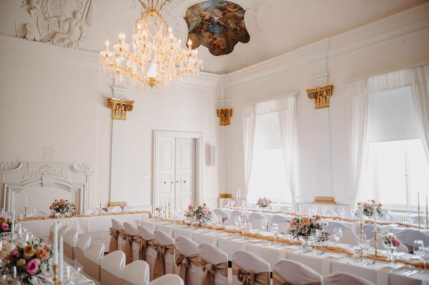 Elegant white ballroom with crystal chandeliers and round tables set for a formal wedding reception.