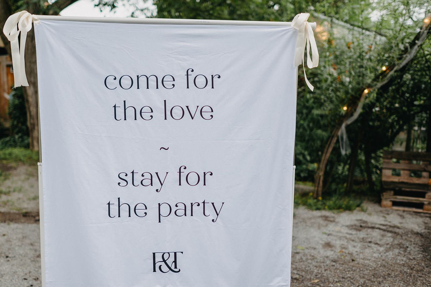 White banners with text hanging between trees at an outdoor wedding venue display romantic messages and signage.