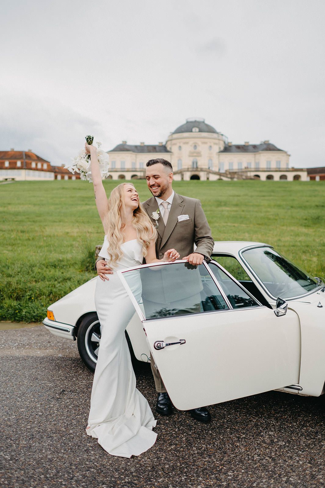 A couple shares joyful moments together beside a classic white convertible car in a scenic outdoor setting.