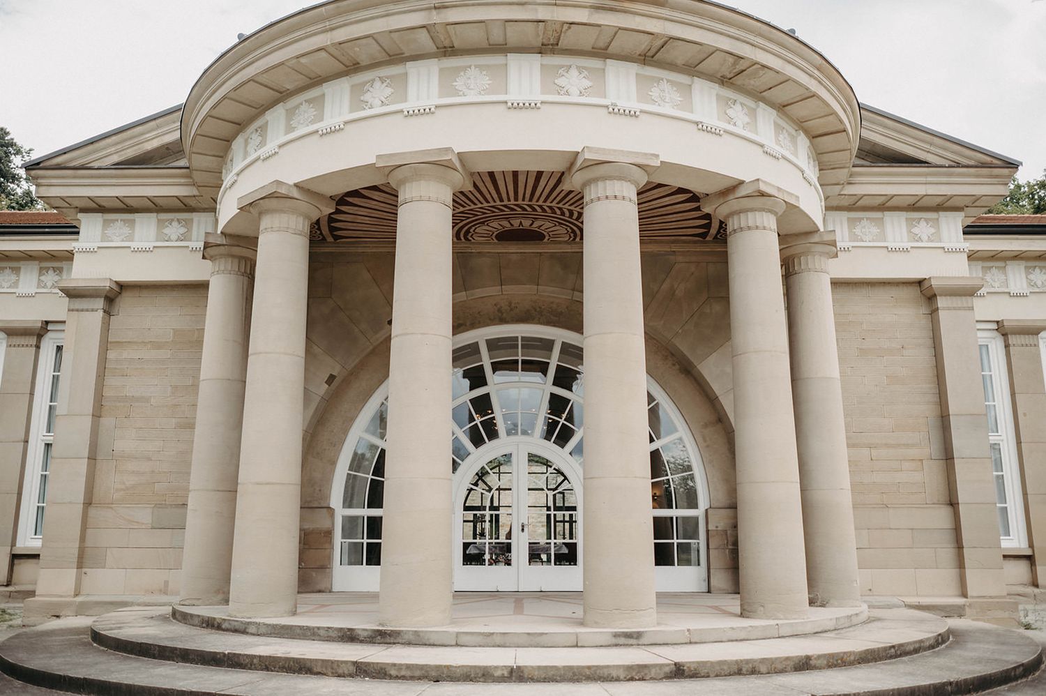 Panoramic view of a neoclassical building entrance with white stone columns and arched windows.