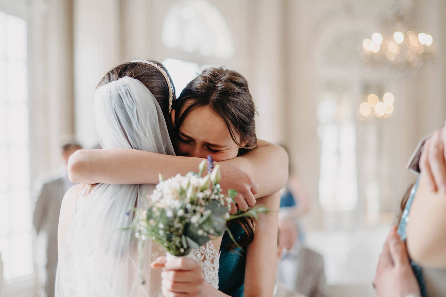 Tender moment between newlyweds sharing their first kiss at an elegant wedding ceremony with chandeliers overhead.