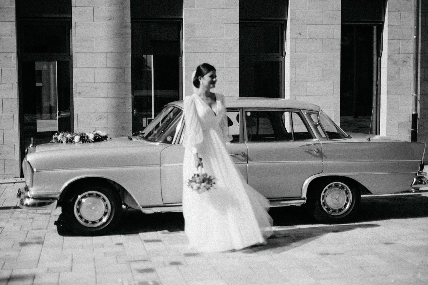 A classic vintage car parked outside a brick building creates an elegant backdrop for wedding photography.
