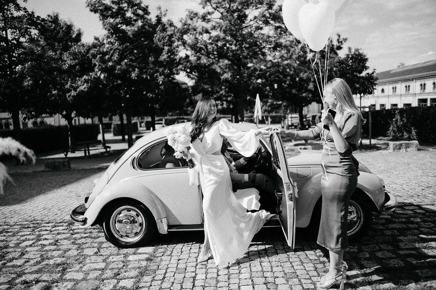 A series of black and white wedding photos showing romantic moments between newlyweds near vintage cars.
