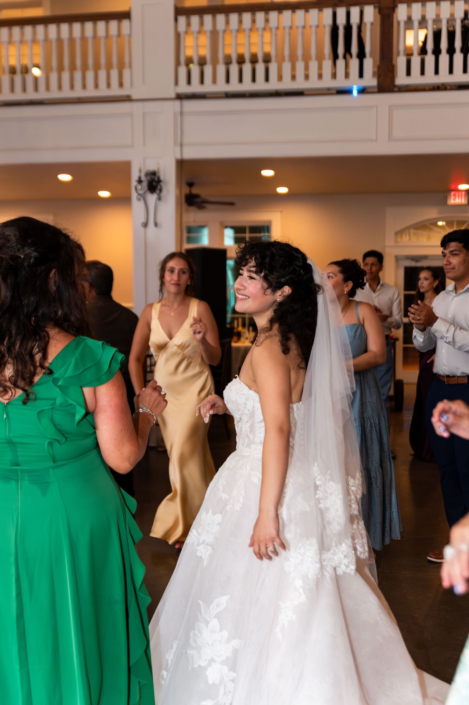 Bride in lace ball gown and veil smiling while dancing with guests at wedding reception.