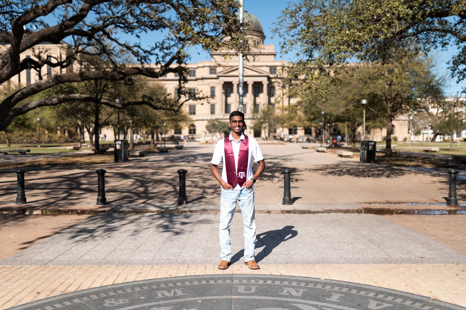 Texas A&M graduate poses on campus compass with iconic domed Academic Building in background.