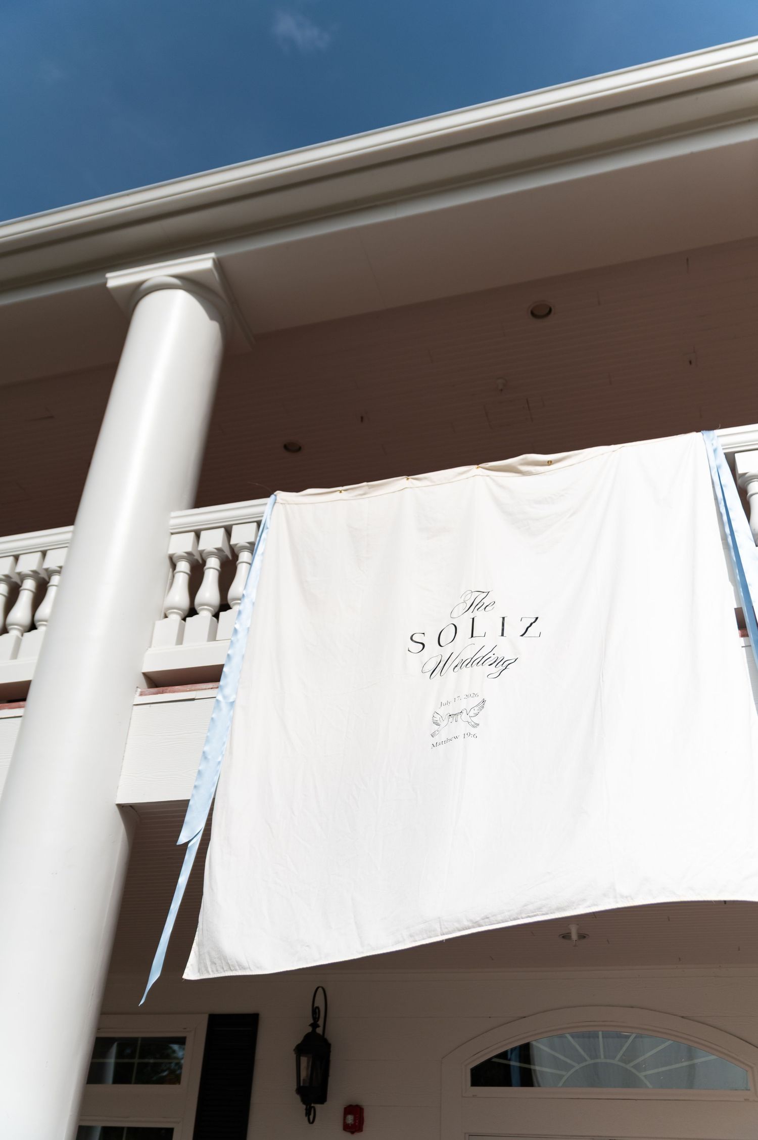 White banner reading The Soliz Wedding hanging from a Southern-style venue balcony against a blue sky.