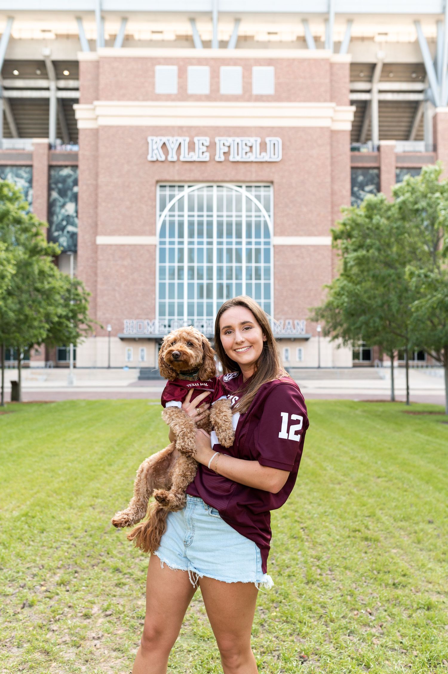 Smiling woman in ATM jersey holds fluffy dog in front of Kyle Field stadium at Texas A&M.