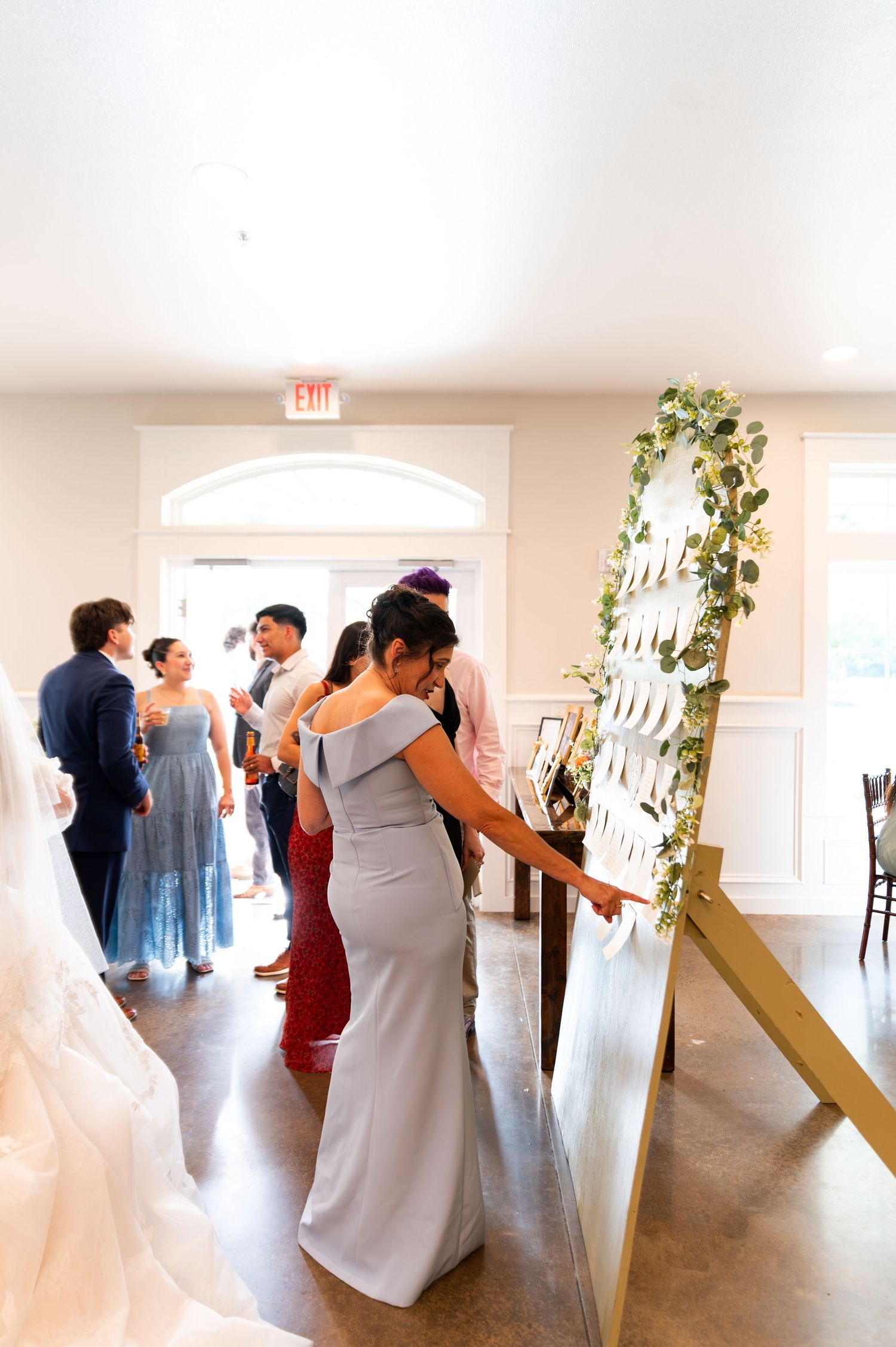 Wedding guests browse seating chart display decorated with greenery garland at elegant reception venue entrance.