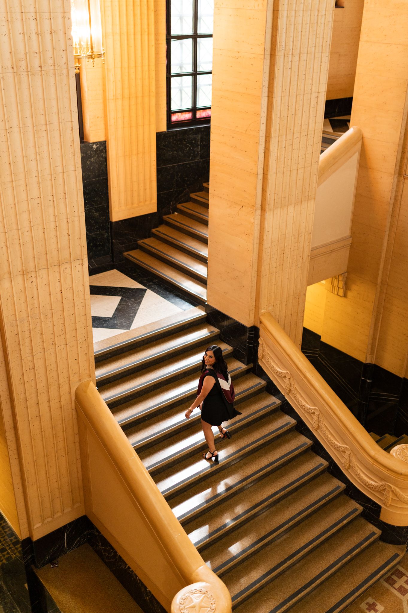 Woman in black dress ascending grand marble staircase in elegant classical building with tall columns. Grad Photos at the Texas A&M Admin