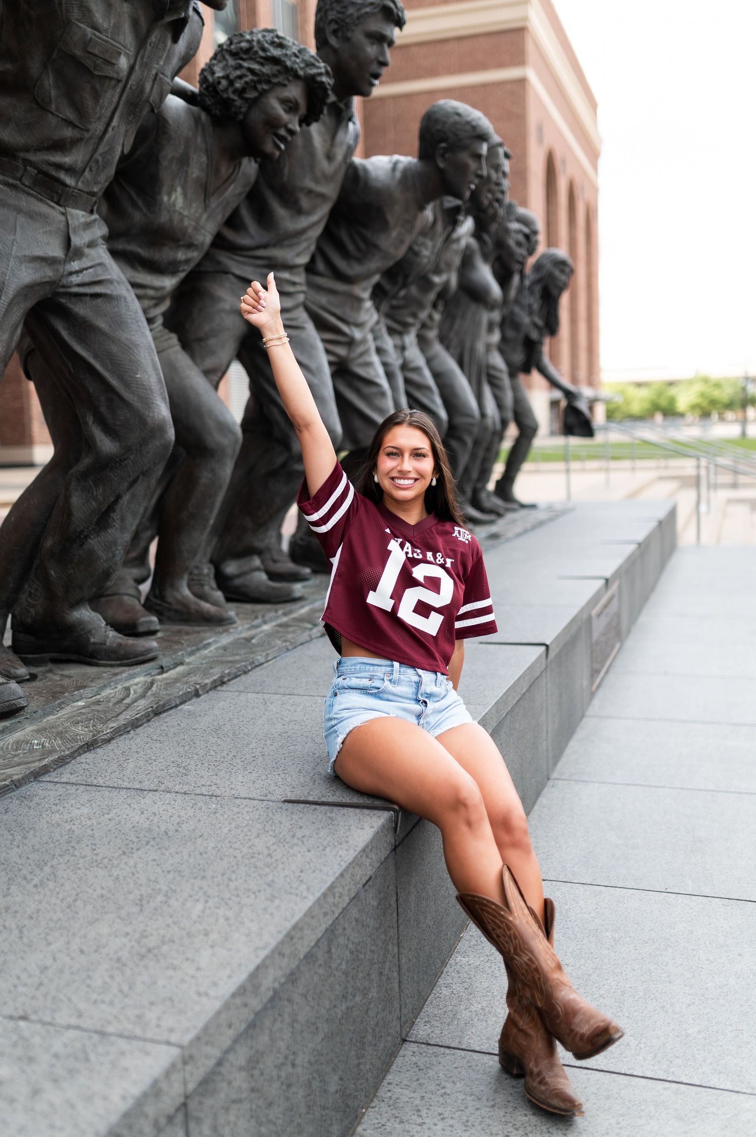 Woman in Texas A&M jersey posing with bronze statues outside Kyle Field stadium.