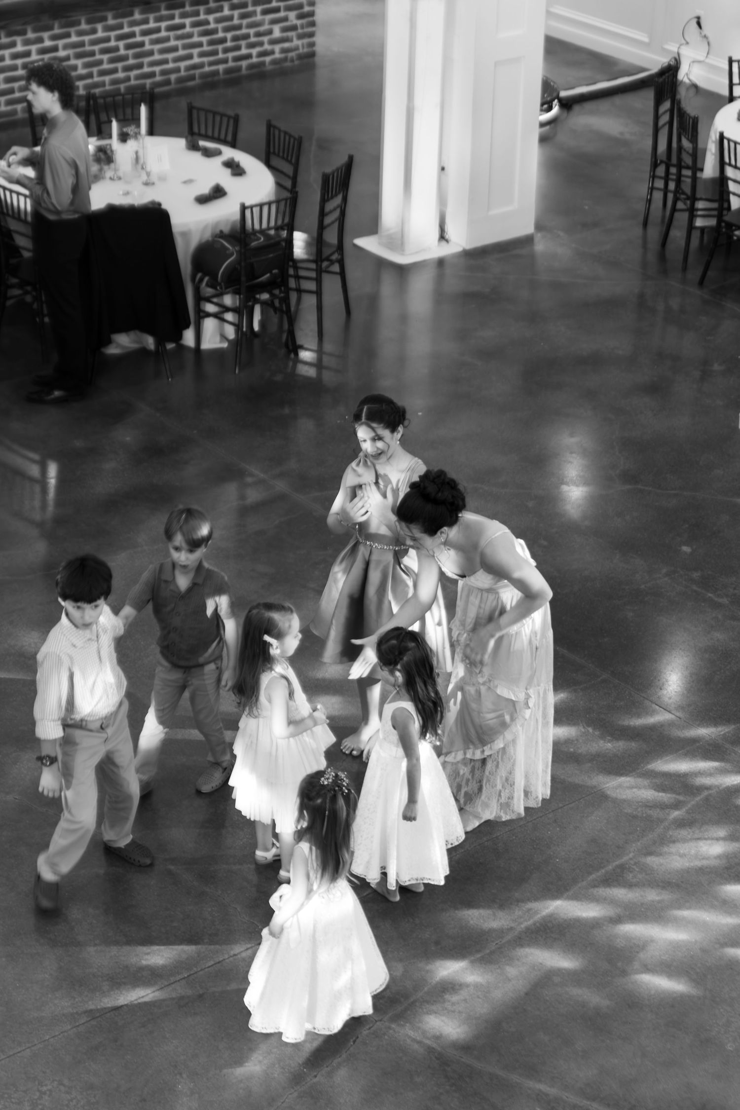 Aerial black and white view of children dancing with guests on wedding reception ballroom dance floor.