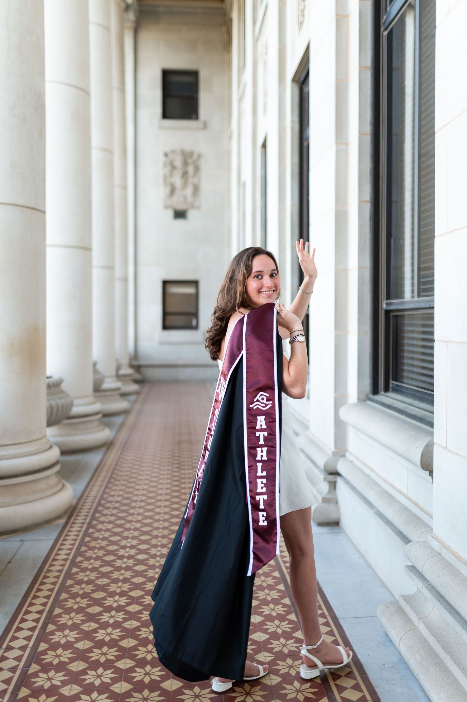Texas A&M graduate holds cap and gown while showing student athlete stole in campus hallway. Grad Photos at the Admin building
