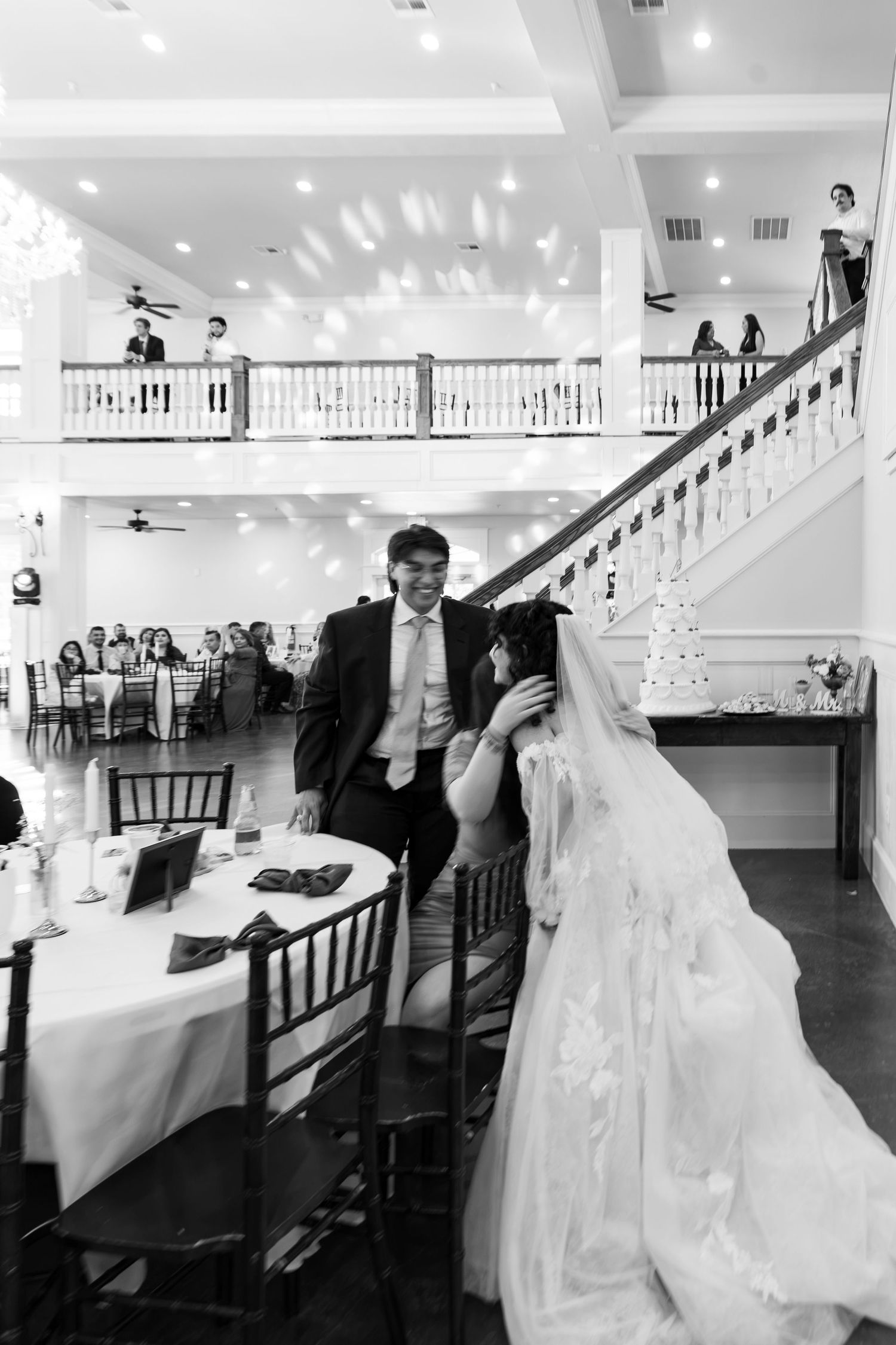 Bride and groom share intimate moment at sweetheart table in grand ballroom wedding reception in black and white.