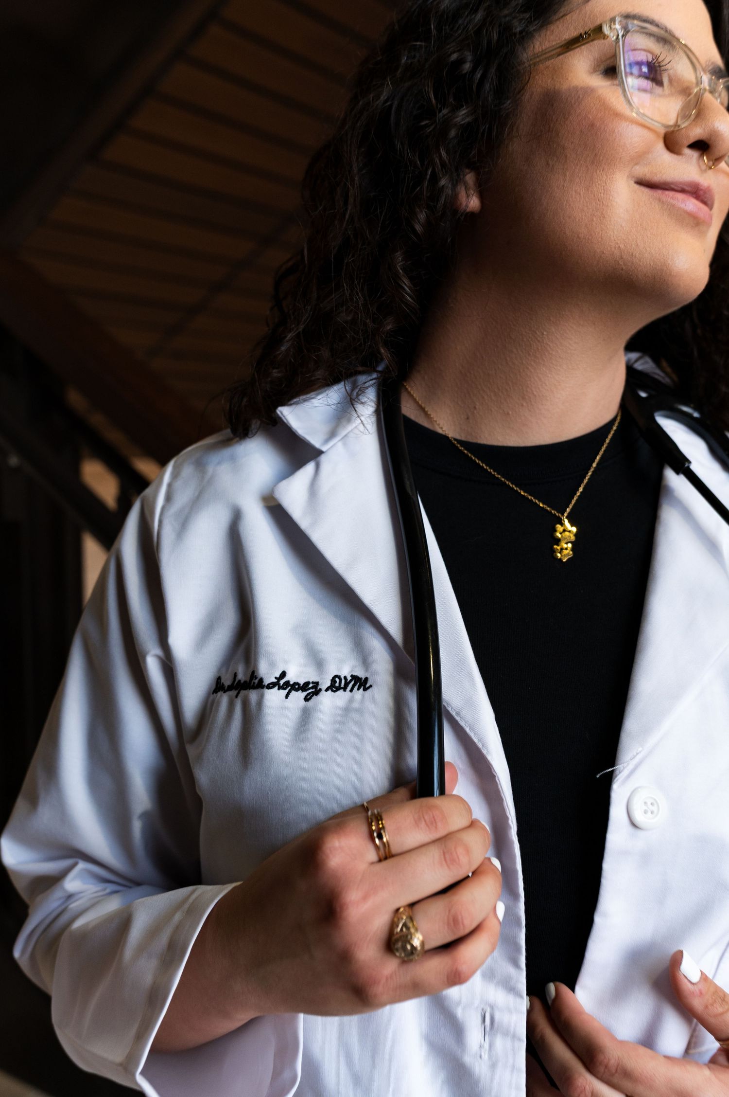 Close-up of female doctor in embroidered white lab coat wearing gold necklace and stethoscope.