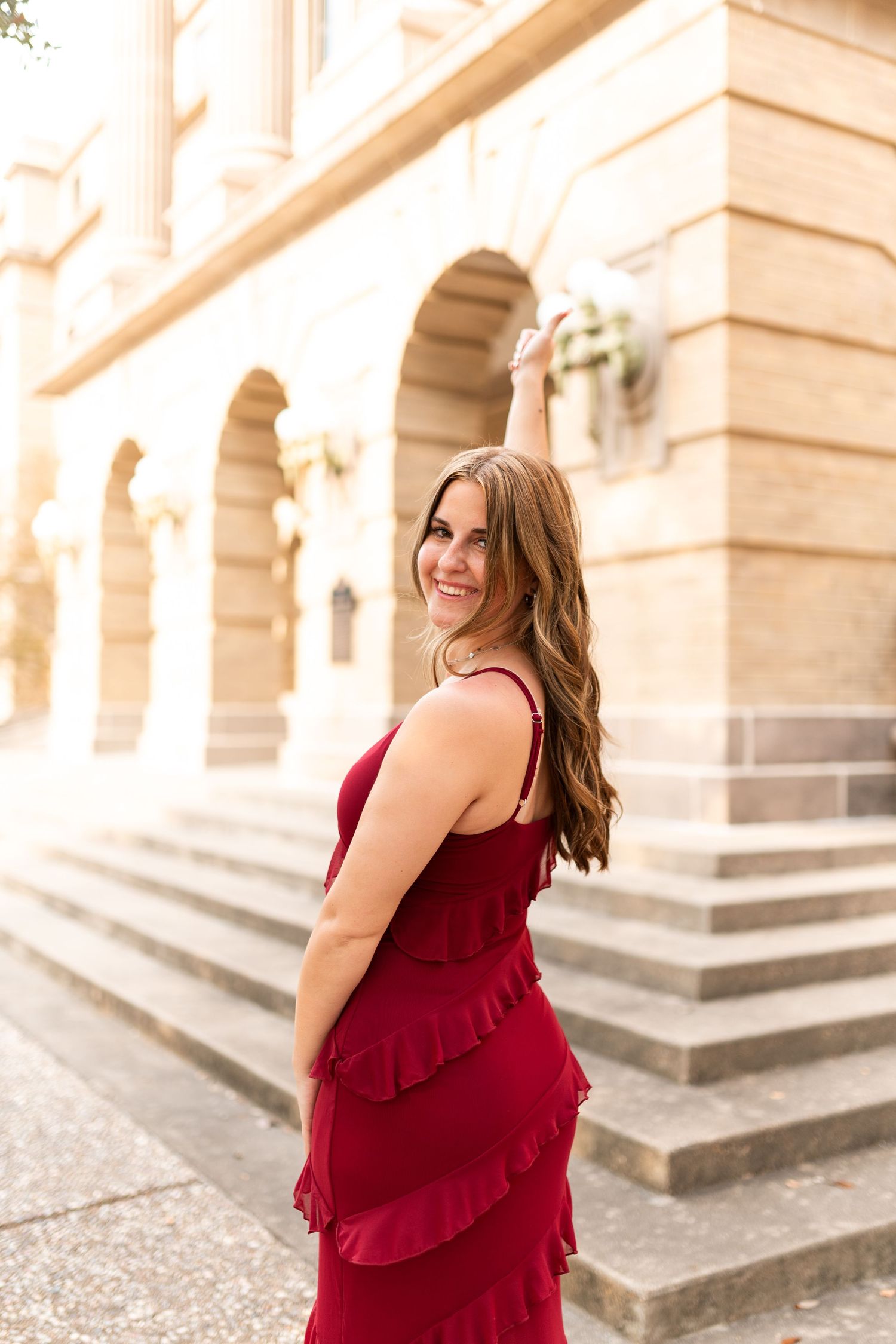 Young woman in red ruffled dress poses on stone steps outside historic building.