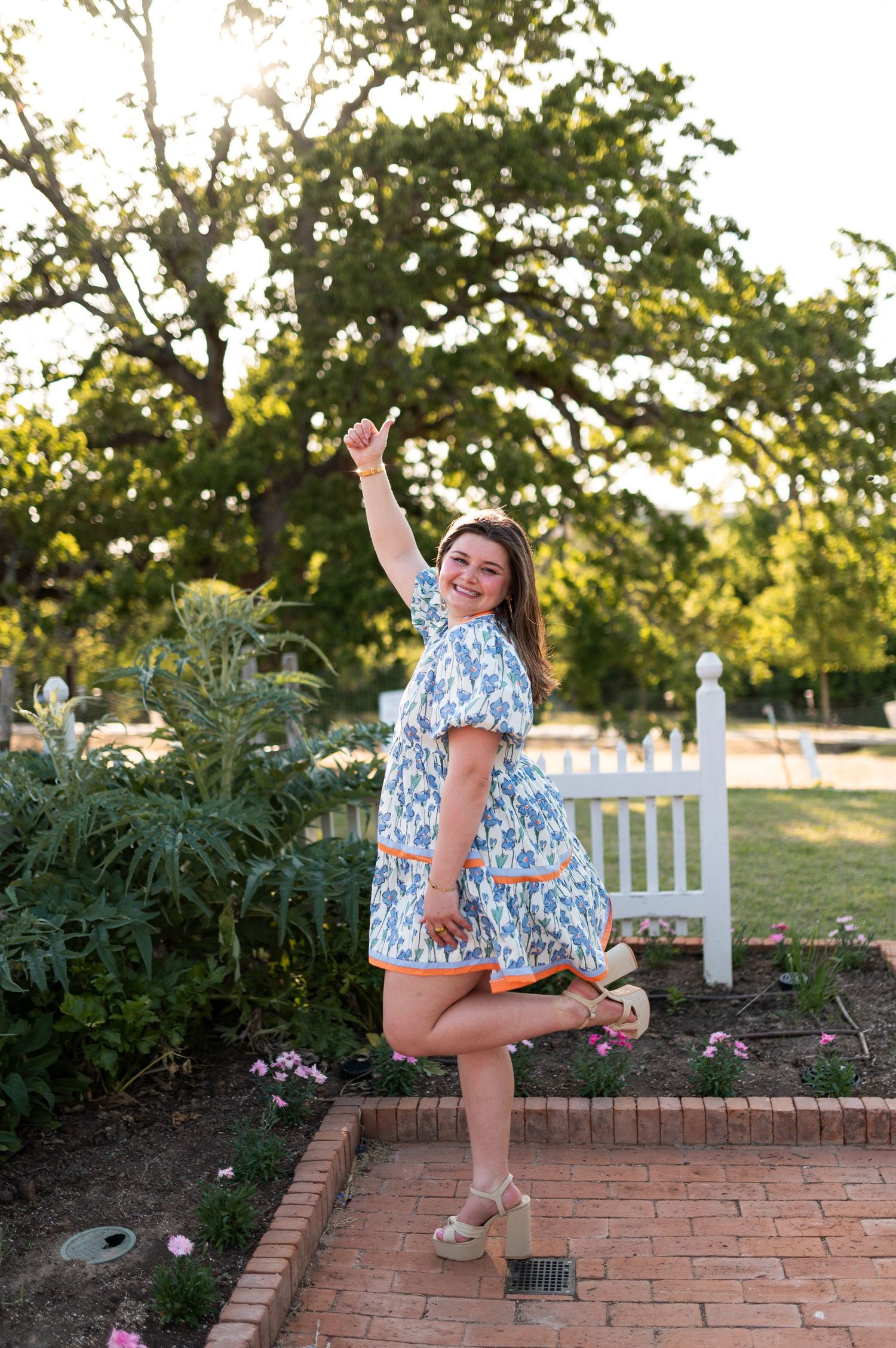 Joyful woman in blue floral dress celebrating with raised fist in sunny garden setting.