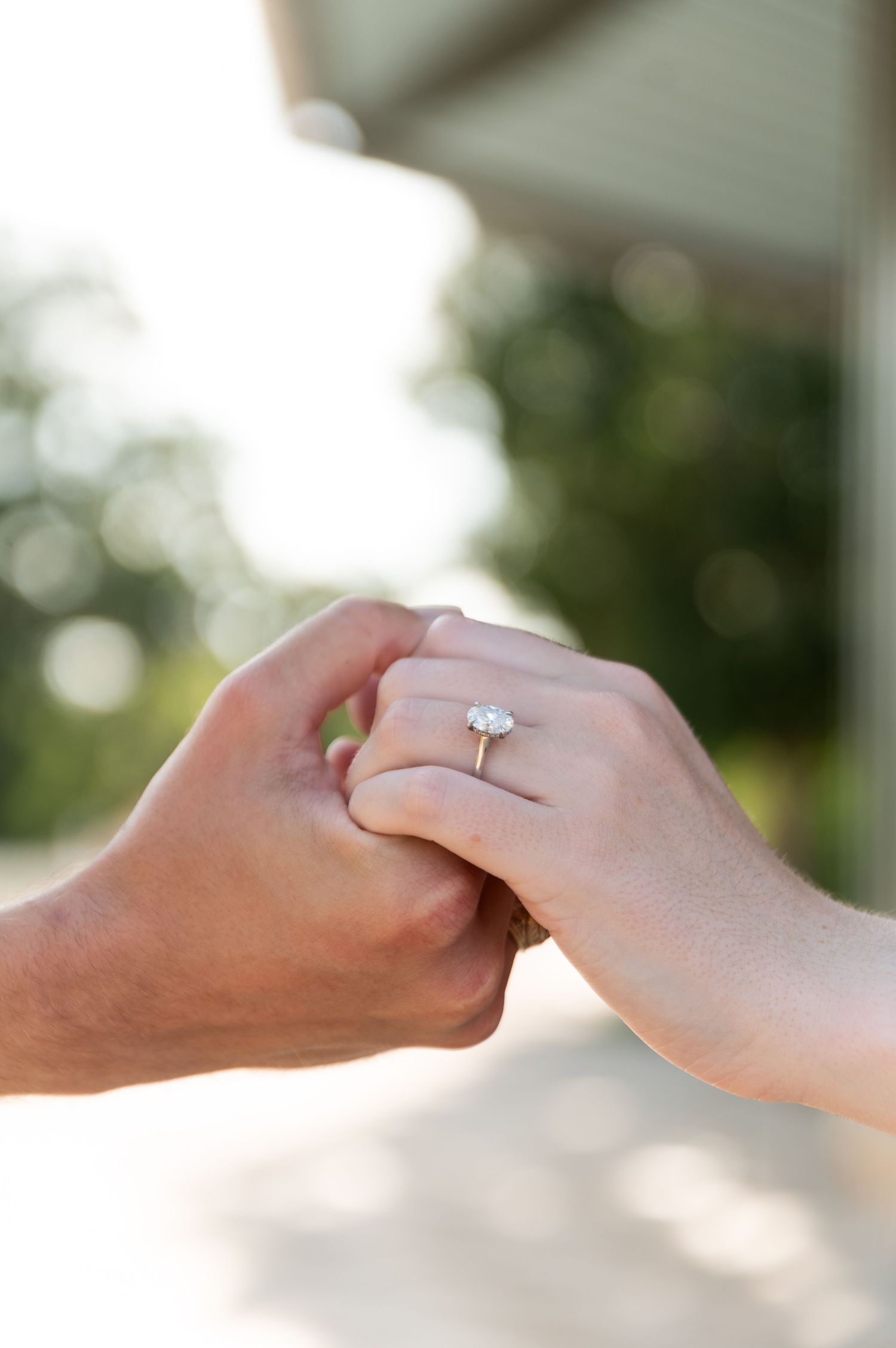 Close-up of two hands holding, featuring a stunning diamond solitaire engagement ring on the bride's finger.