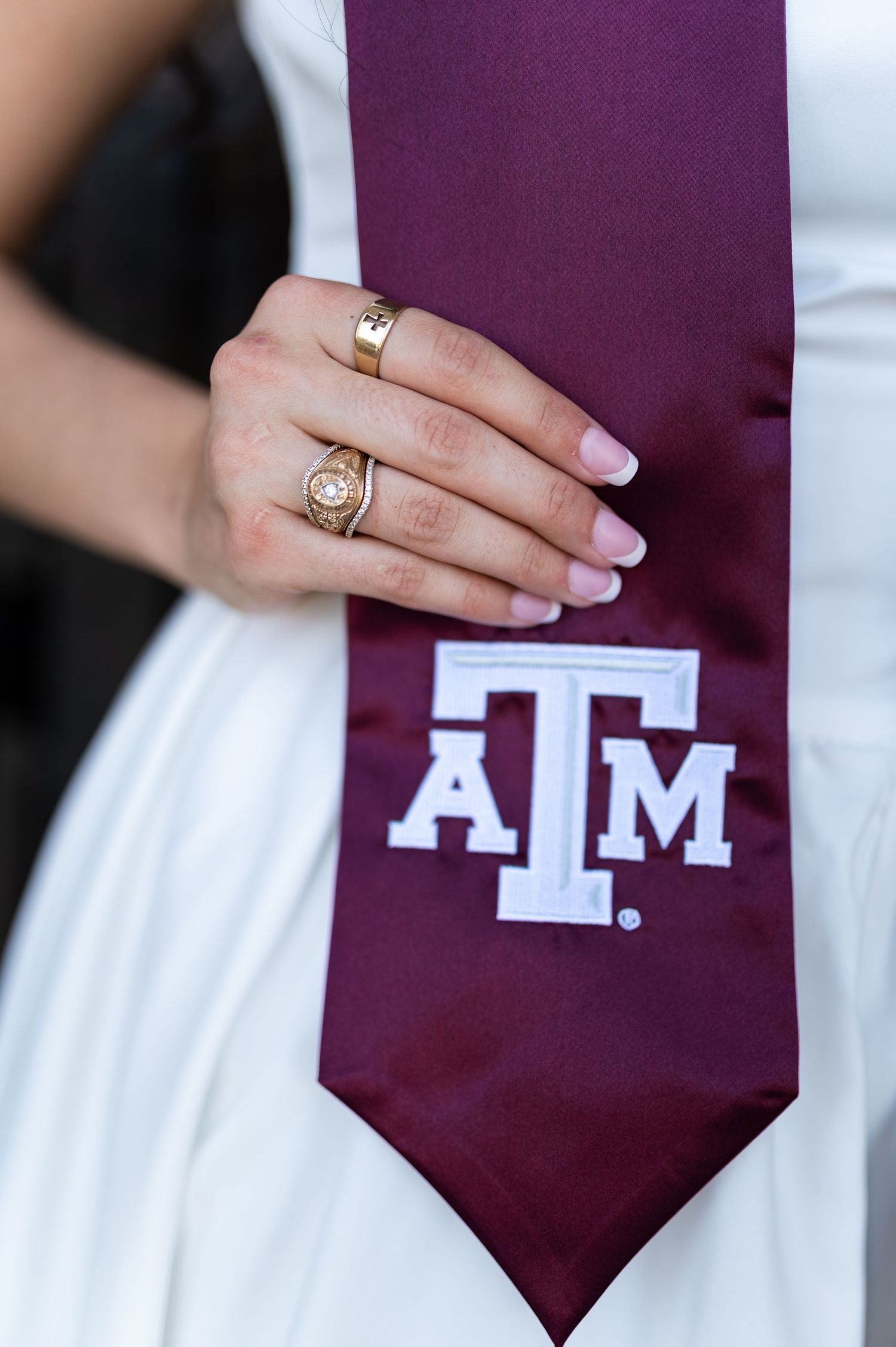 Close-up of a hand wearing gold rings holding a maroon Texas A&M graduation stole. Grad Photos at the Admin building