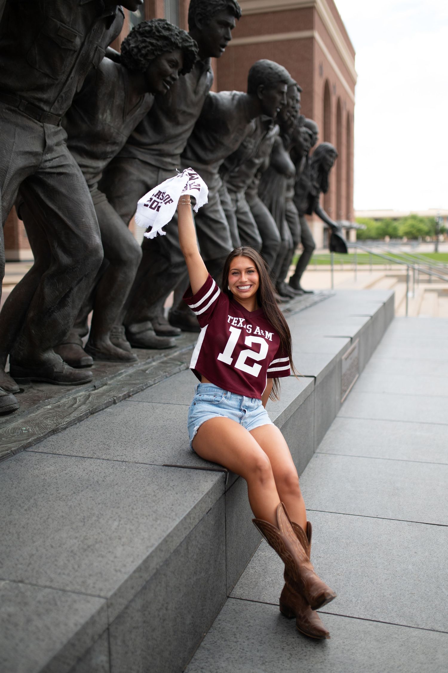 Woman in Texas A&M number 12 jersey poses with bronze statues outside Kyle Field.