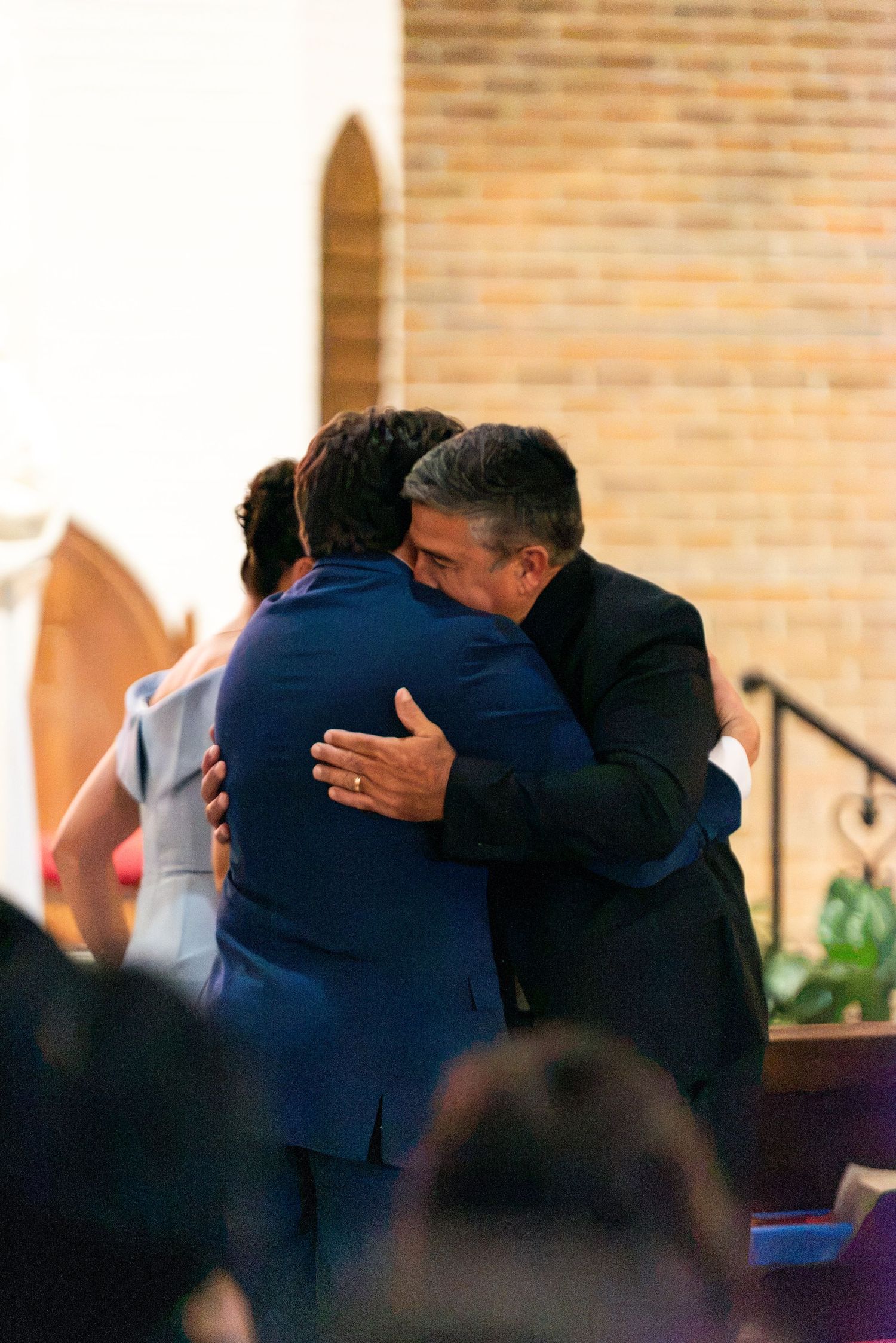 Emotional embrace between two men in suits during heartfelt wedding ceremony moment.