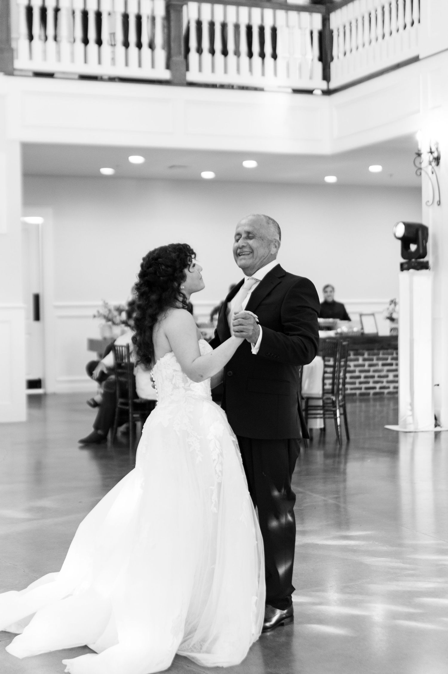 Black and white photo of bride sharing emotional father-daughter dance at wedding reception.