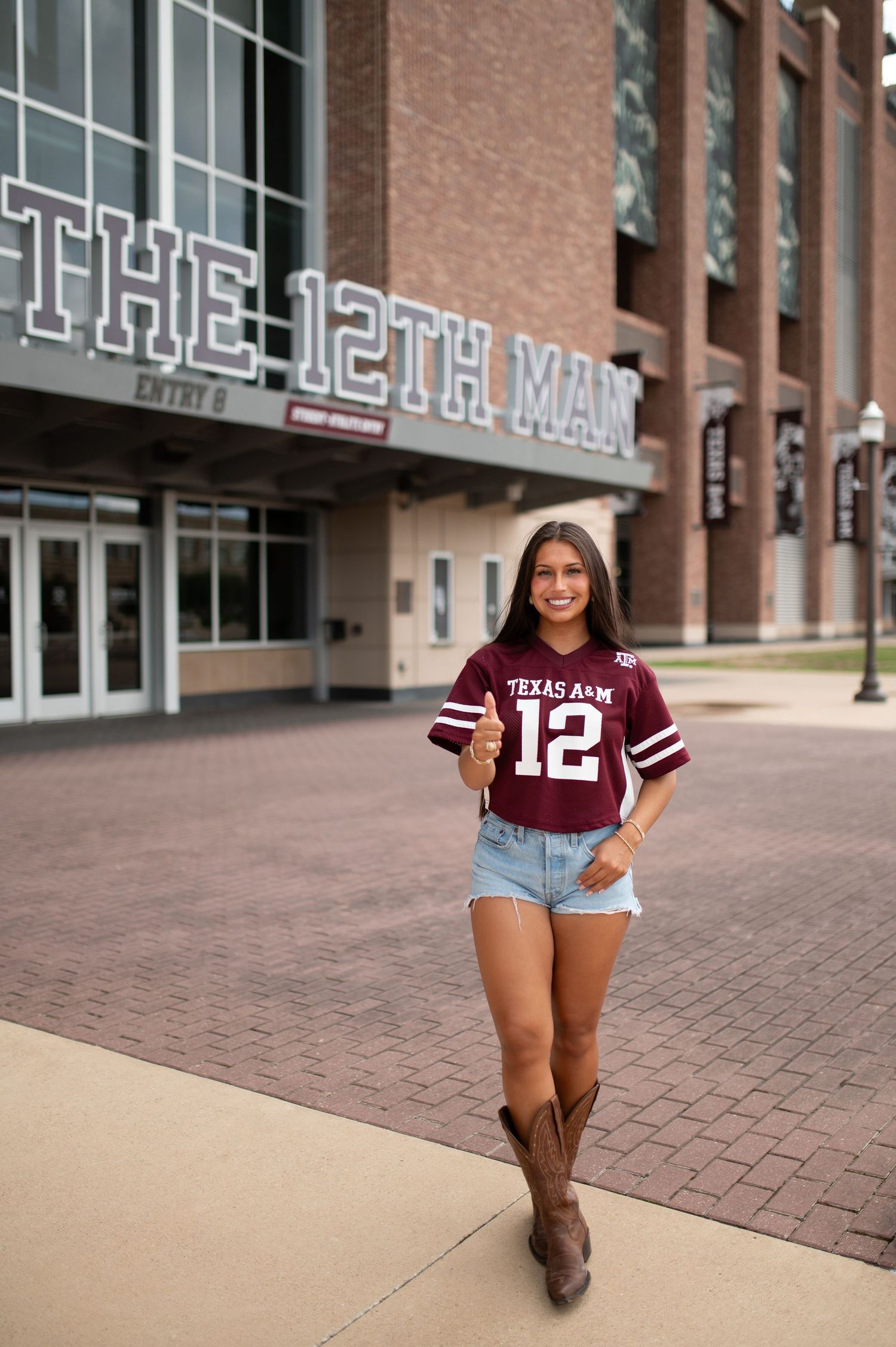 Woman in Texas A&M number 12 jersey poses outside The 12th Man entrance at Kyle Field.