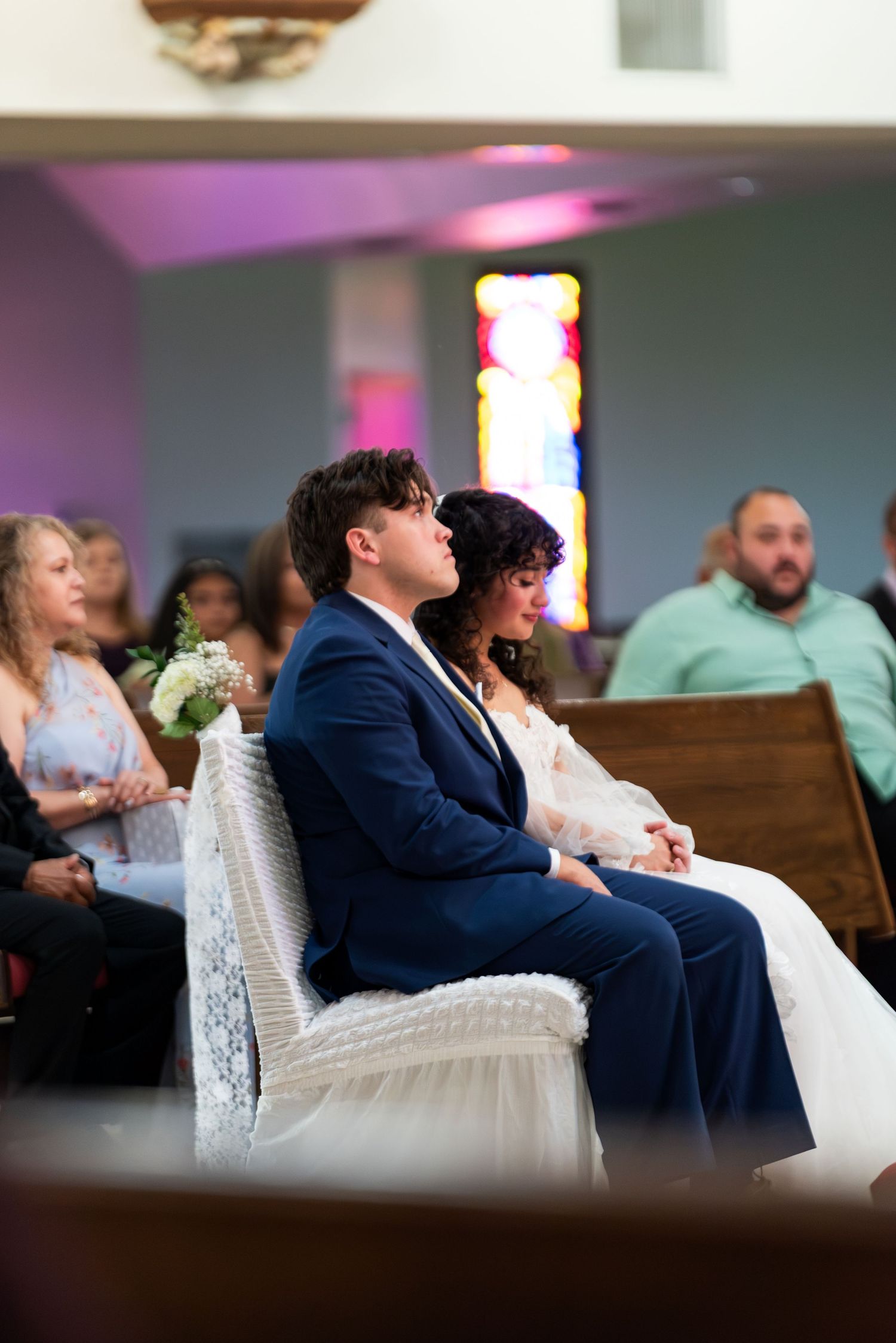 Bride and groom sit together at church altar during wedding ceremony with guests seated in pews behind.