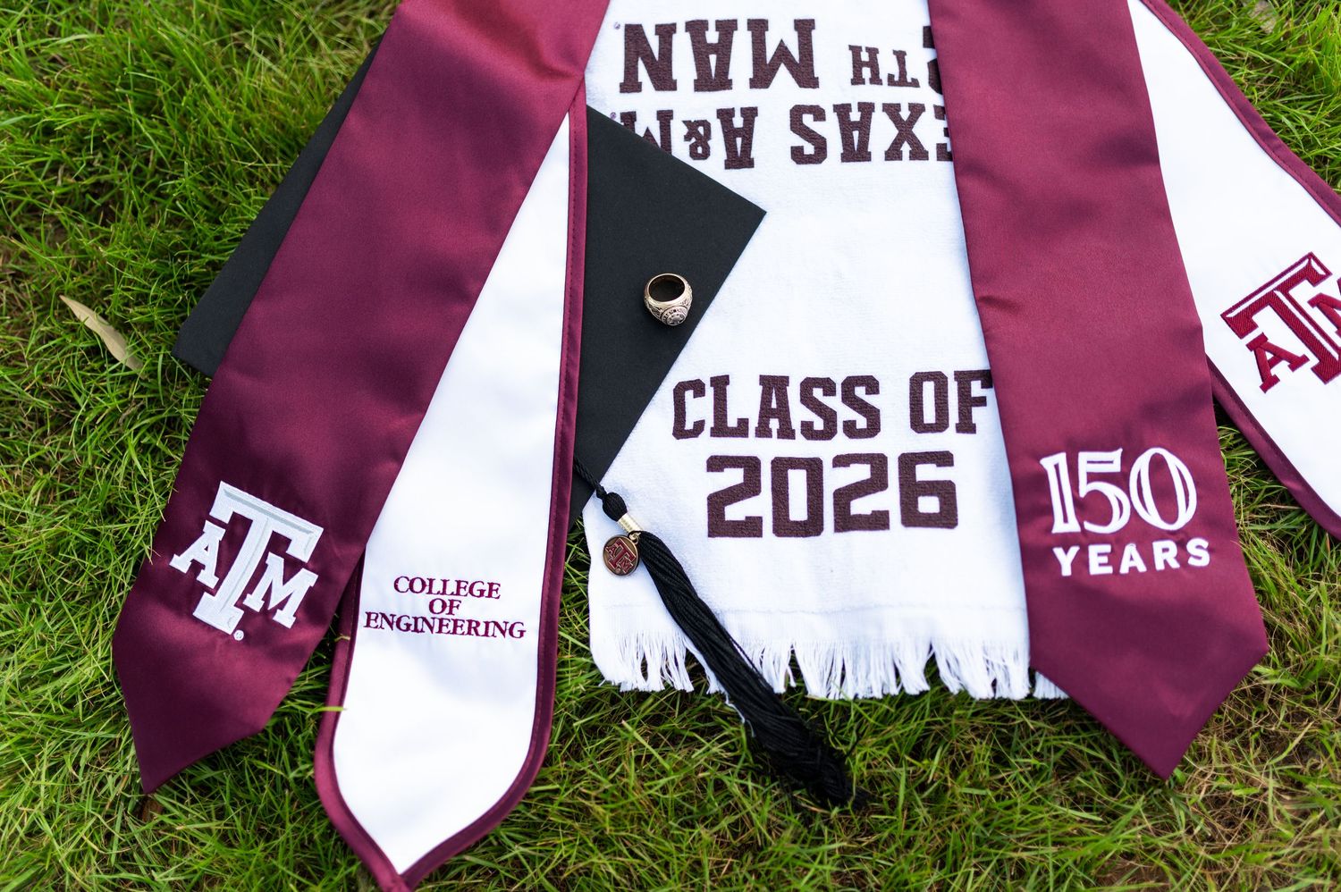 Texas A&M Class of 2026 graduation stoles and cap on grass, 150 years. Grad Photos at the Admin building