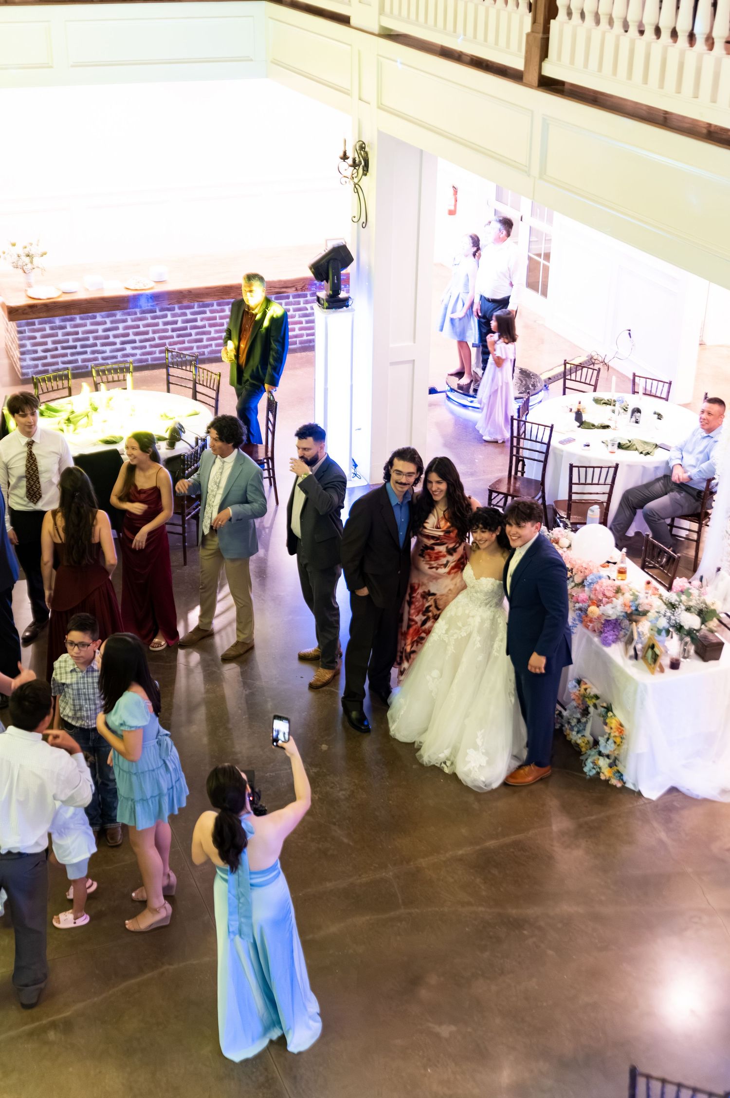 Overhead view of bride and groom posing for photos with guests at wedding reception venue.
