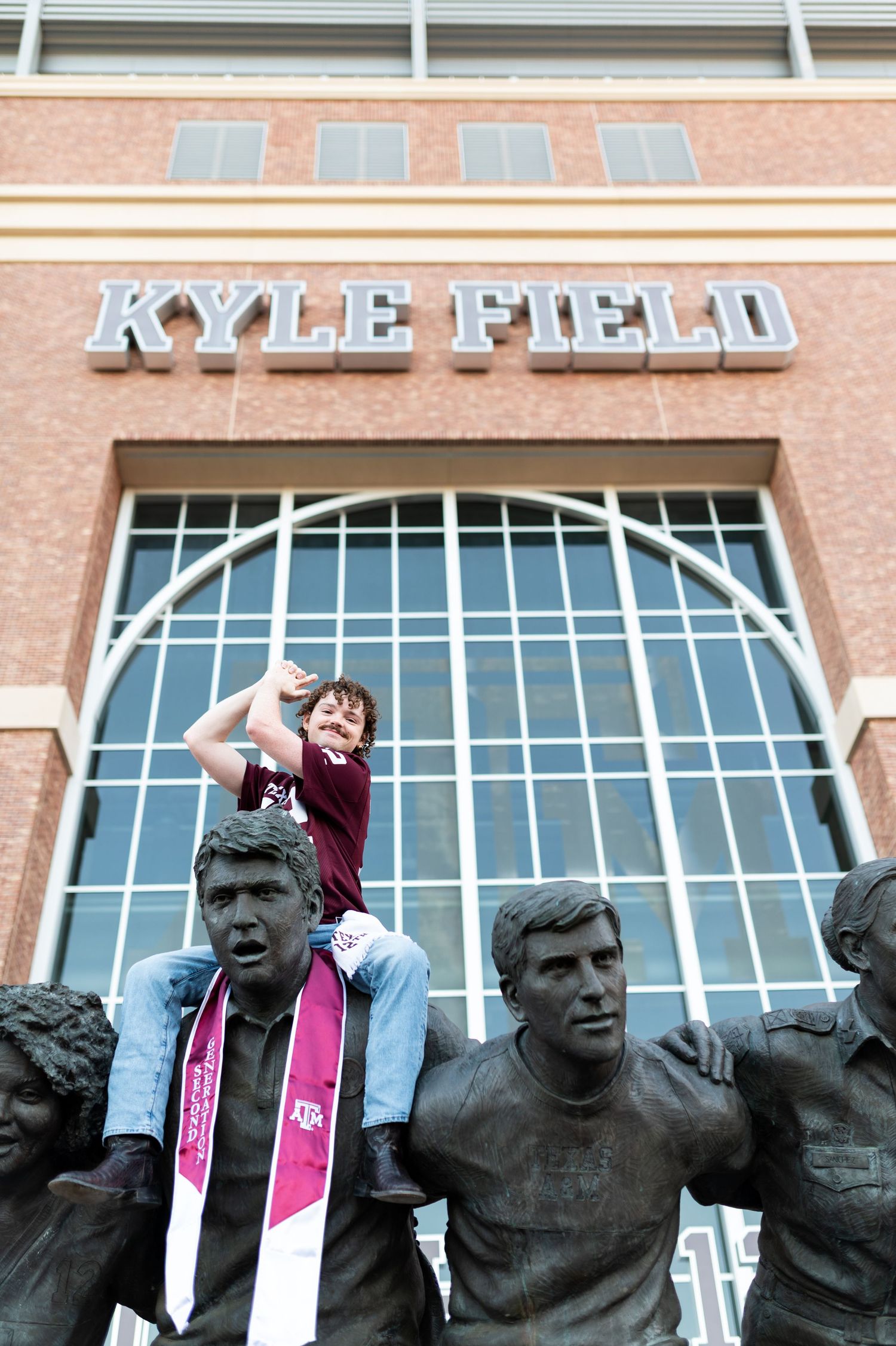 Young boy sits atop bronze statues wearing Texas A&M stole outside Kyle Field.