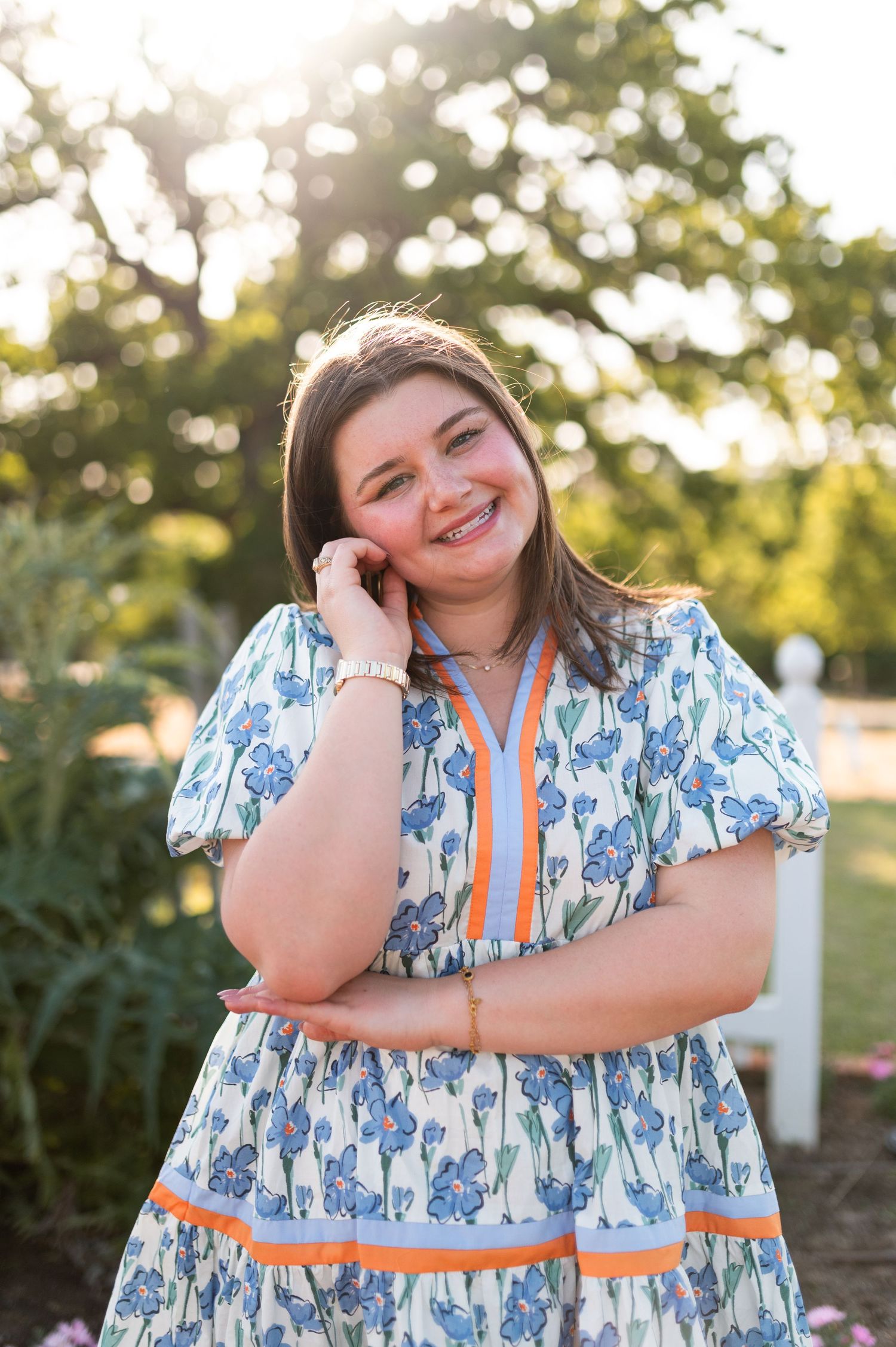 Smiling woman in blue floral dress with orange trim posing in golden hour garden light.