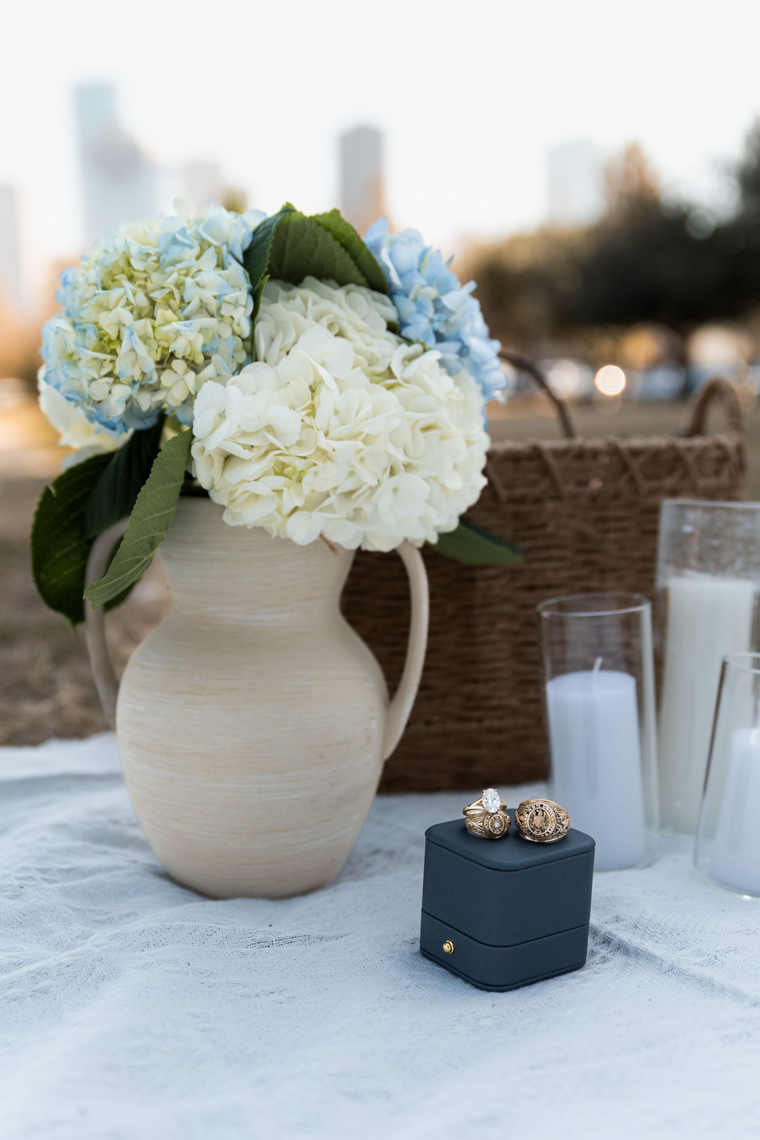 White and blue hydrangea bouquet in ceramic vase beside ring box at outdoor proposal setup.