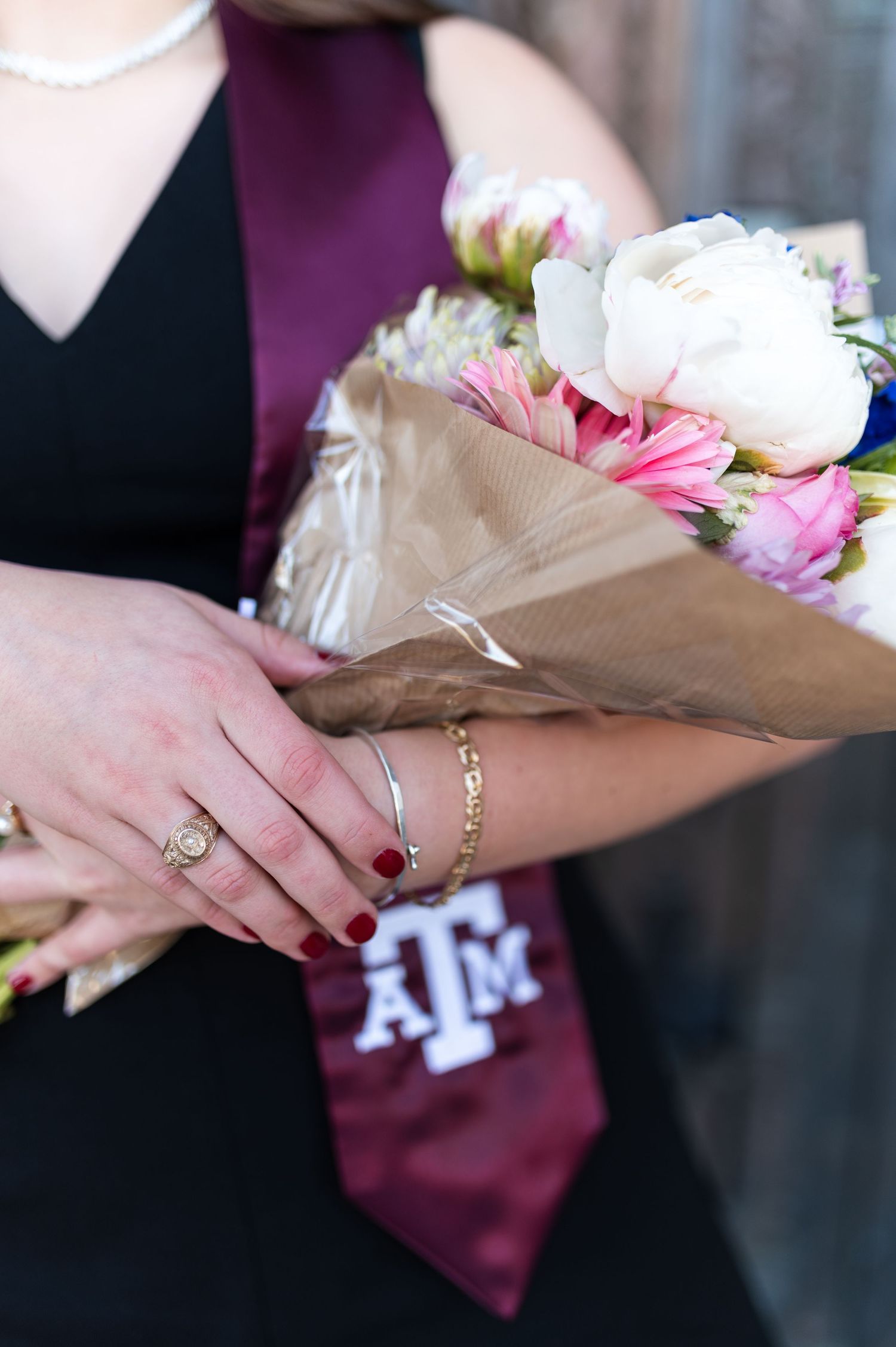 Close-up of hands holding pink and white flower bouquet with Texas A&M graduation stole. Texas A&M Grad Photos at the Admin building