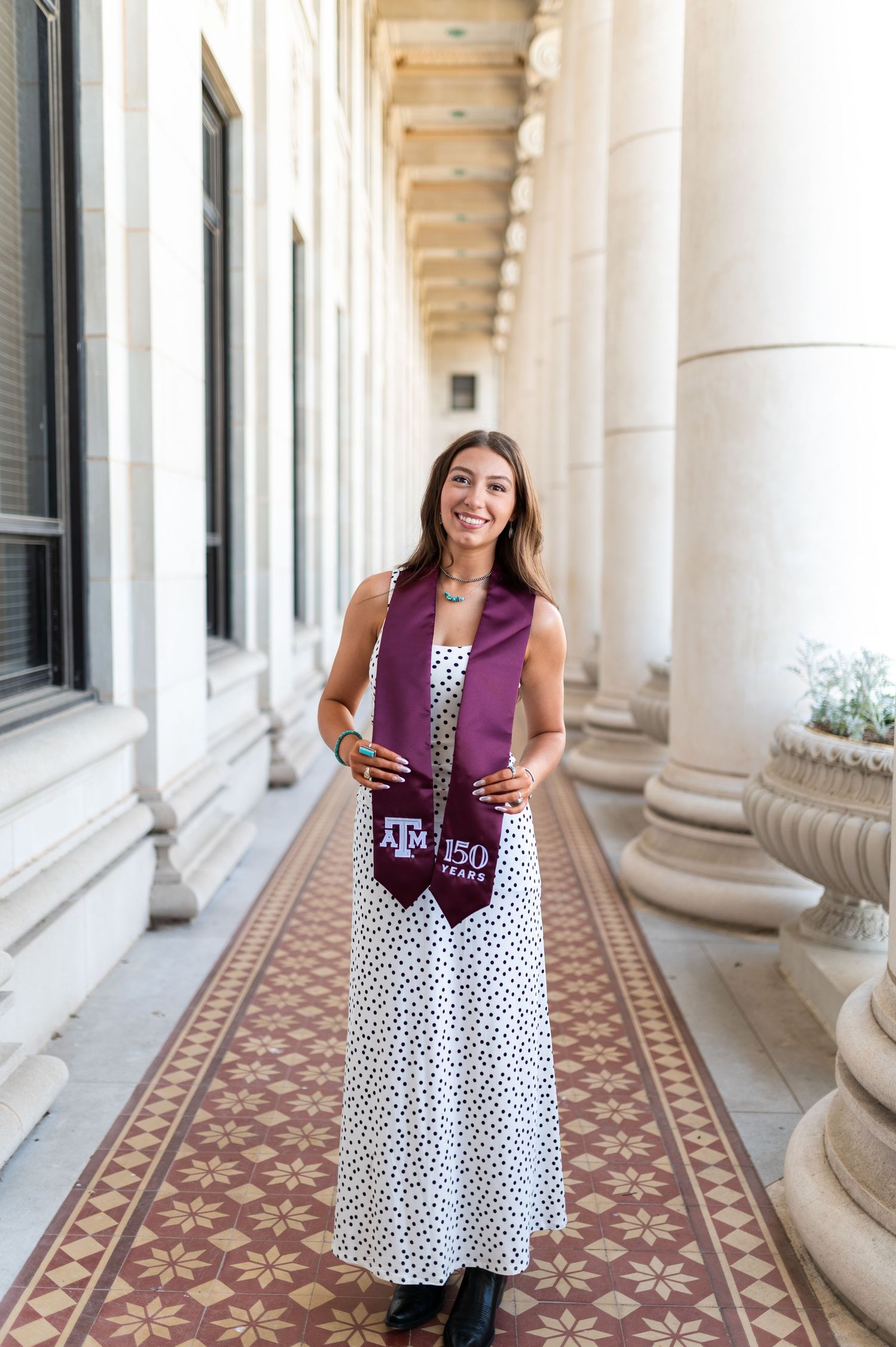 Woman in polka dot dress with Texas A&M 150 Years maroon stole in colonnade. Grad Photos at the Admin building