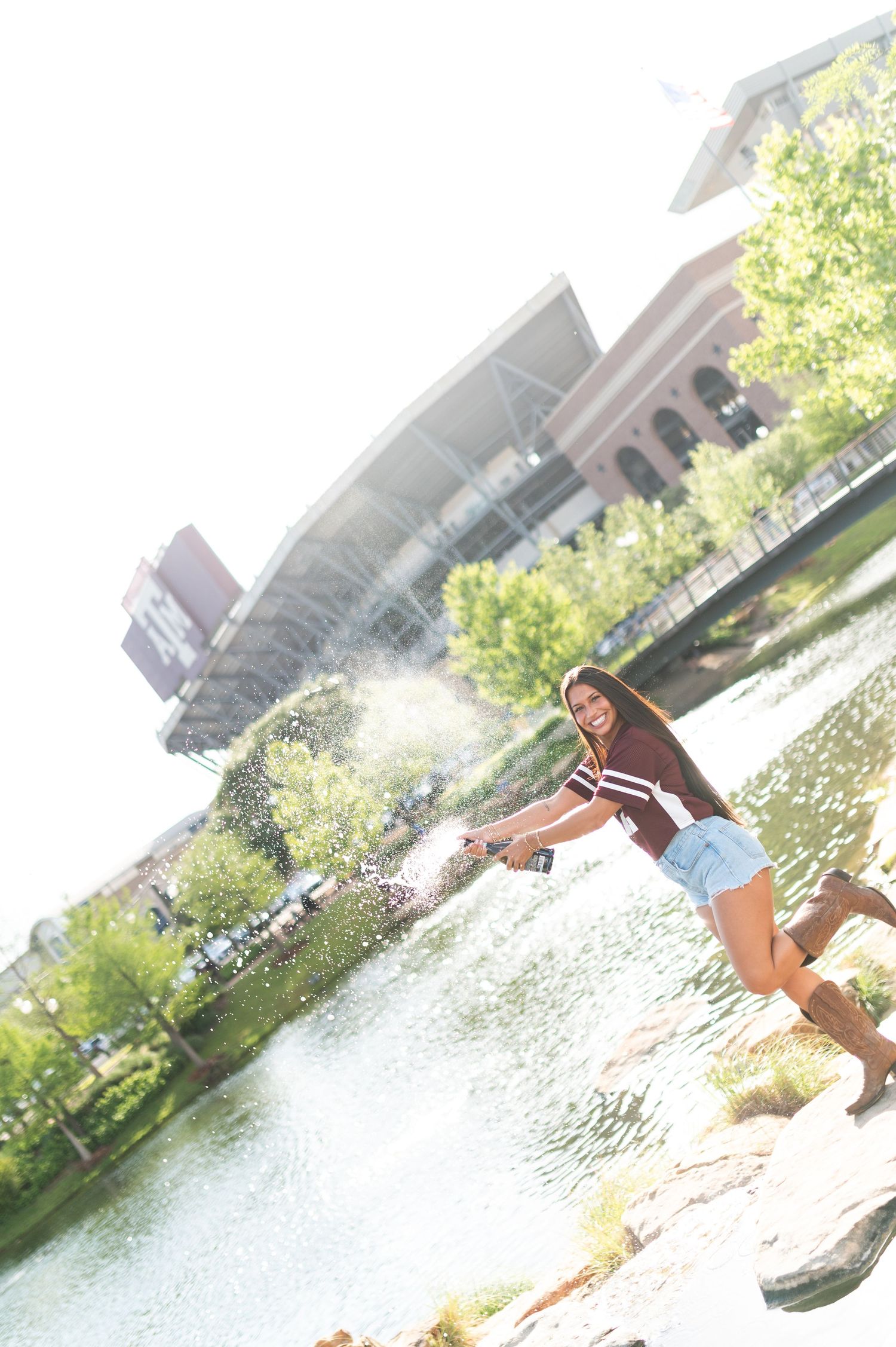 Texas A&M fan in maroon jersey skips stones by a pond near Kyle Field stadium.