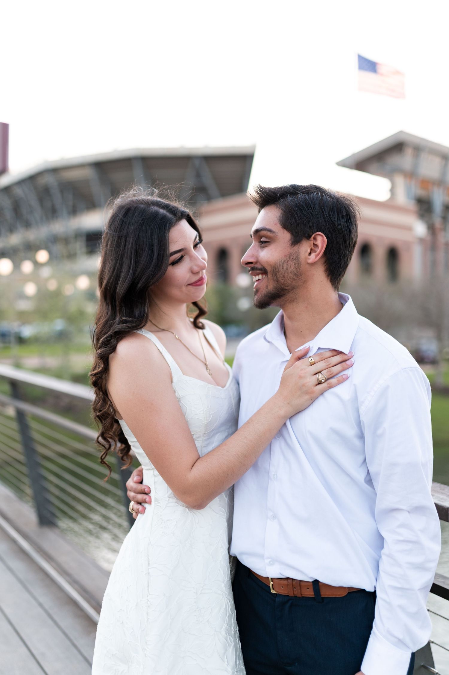 Young couple in white outfits share a romantic moment on bridge near Texas A&M stadium.